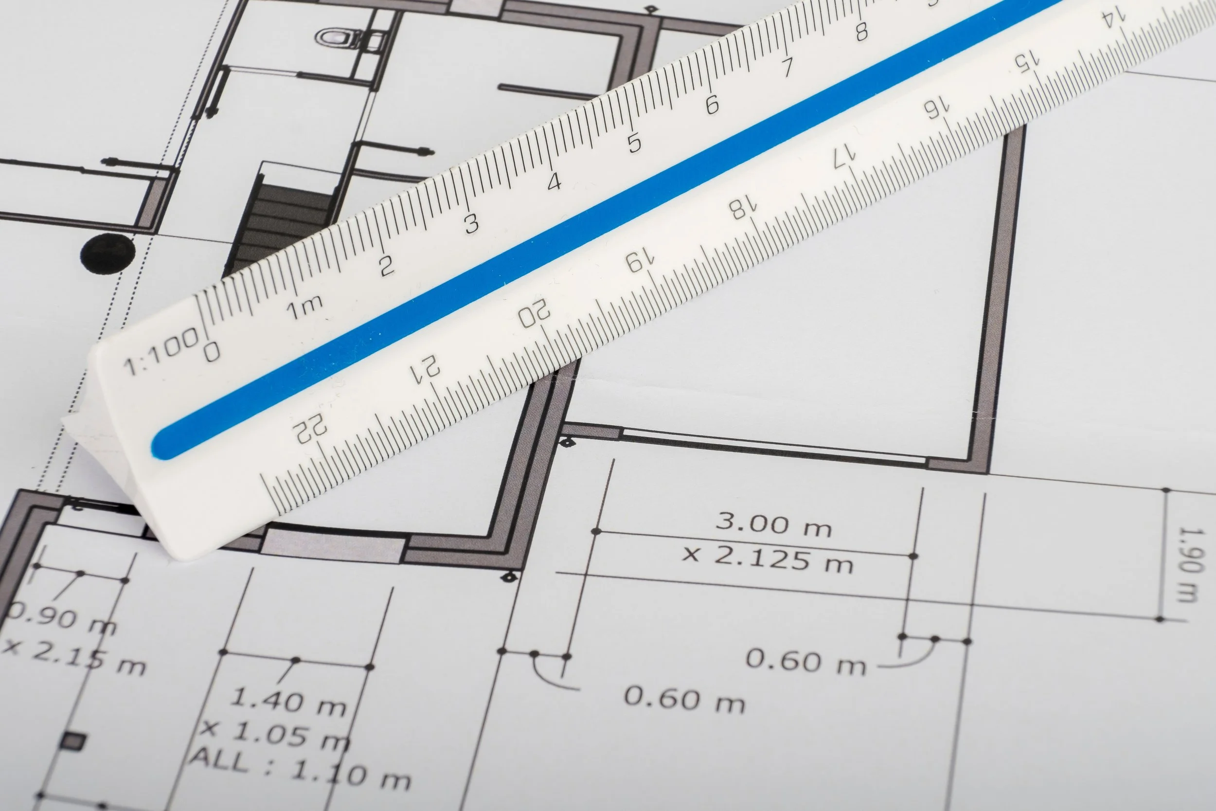 Une règle de mesurage posée sur un plan d'architecture en noir et blanc.