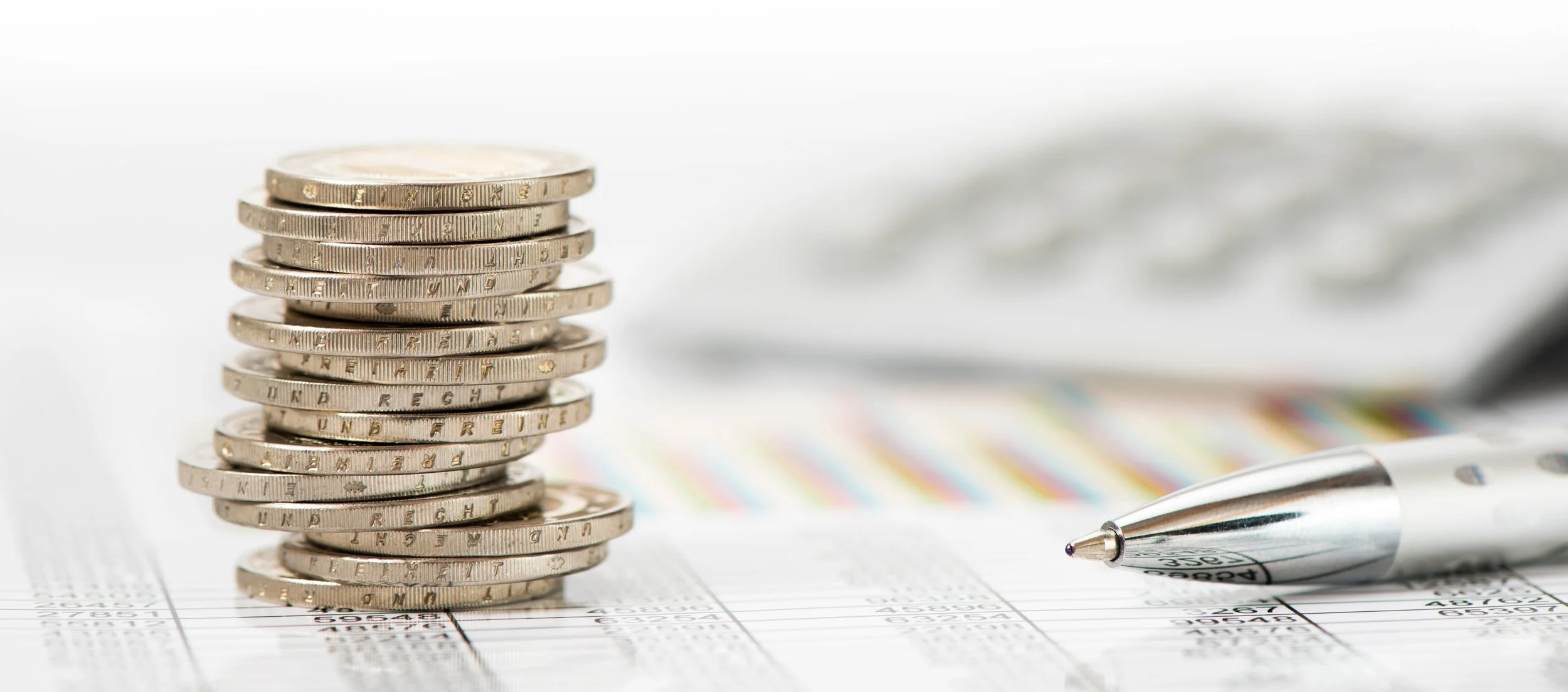 Pièces de monnaie empilées, un stylo et un rapport financier ou un document financier en arrière-plan.