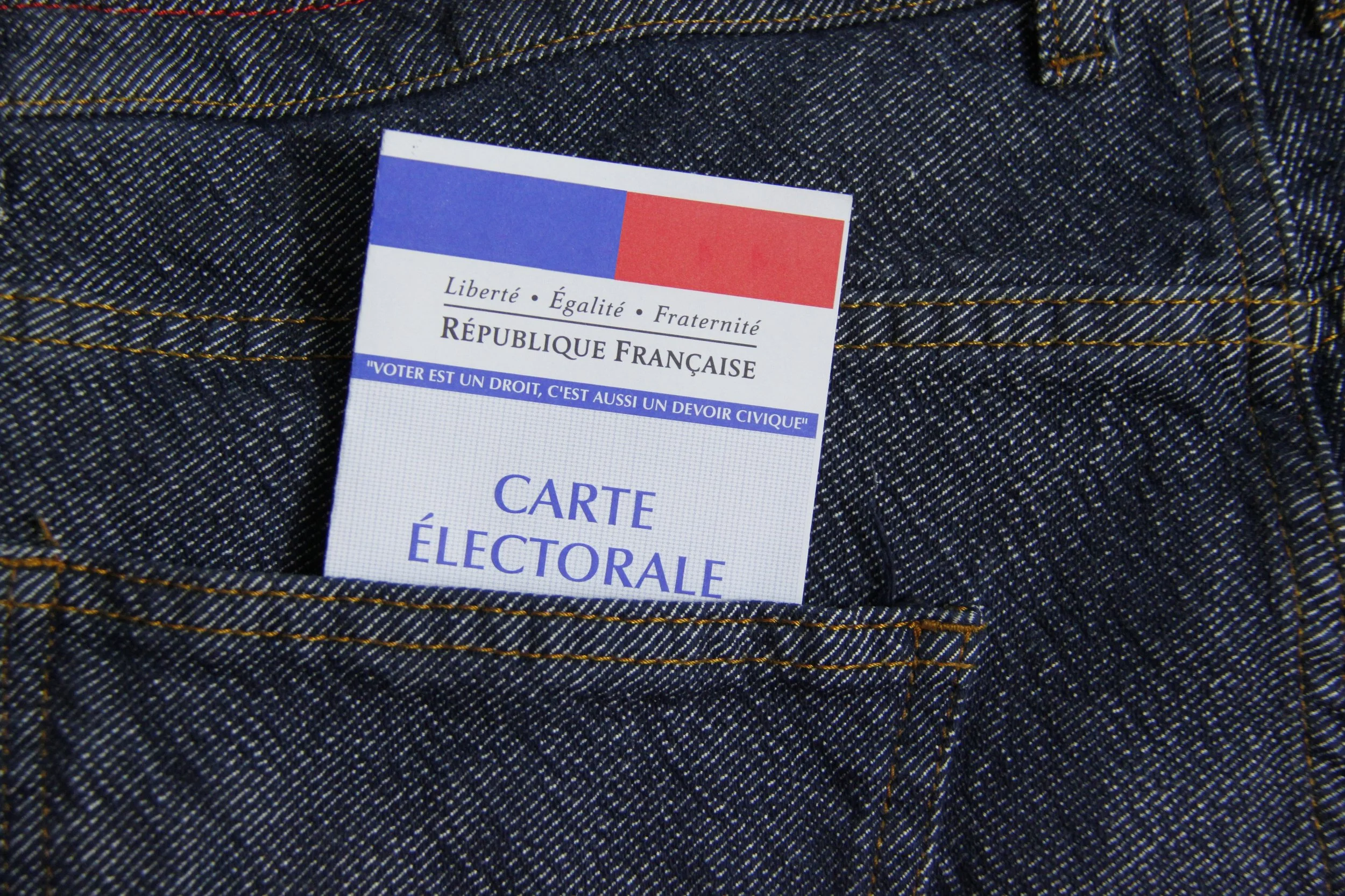 Carte électorale placée dans la poche d'une veste en denim avec couture orange.