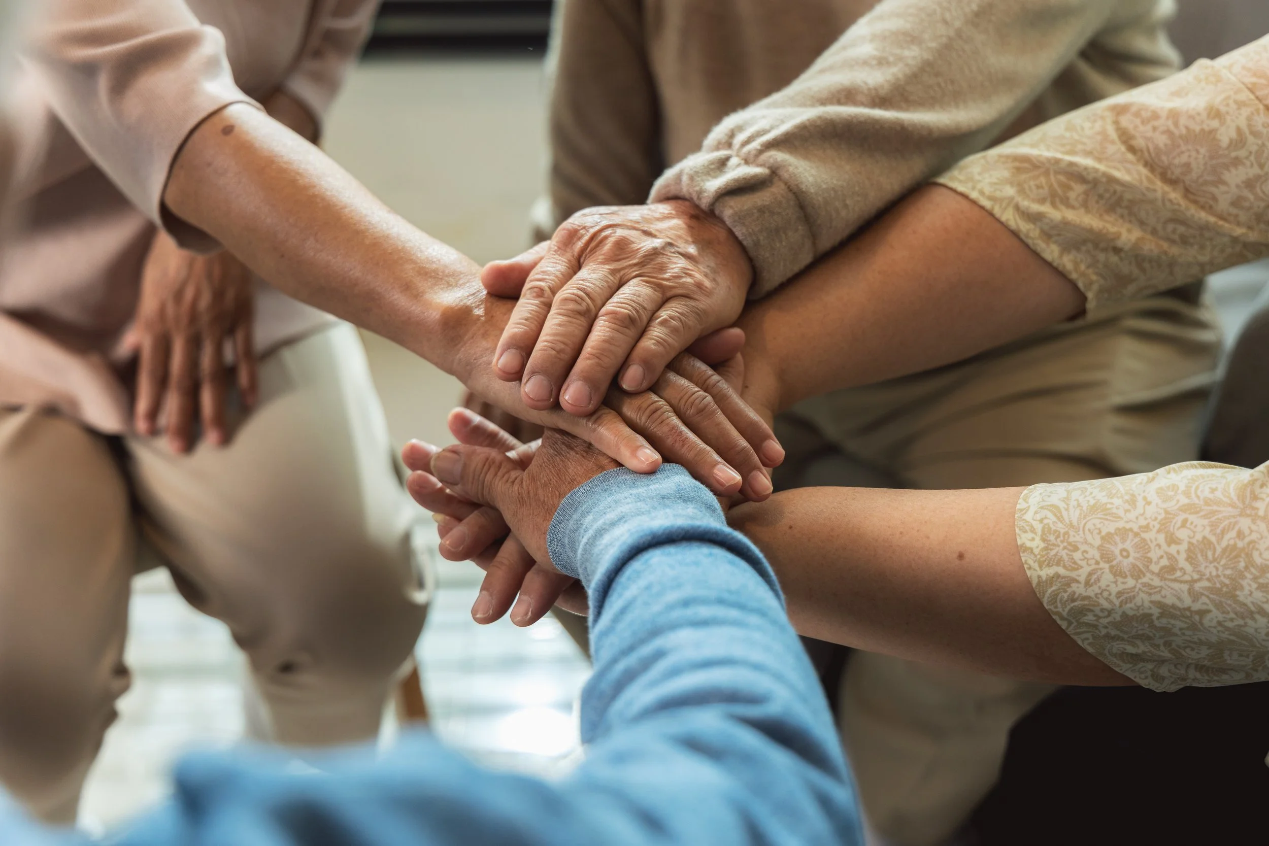 Groupe de personnes de différents âges joignant leurs mains pour un geste de soutien et de solidarité.