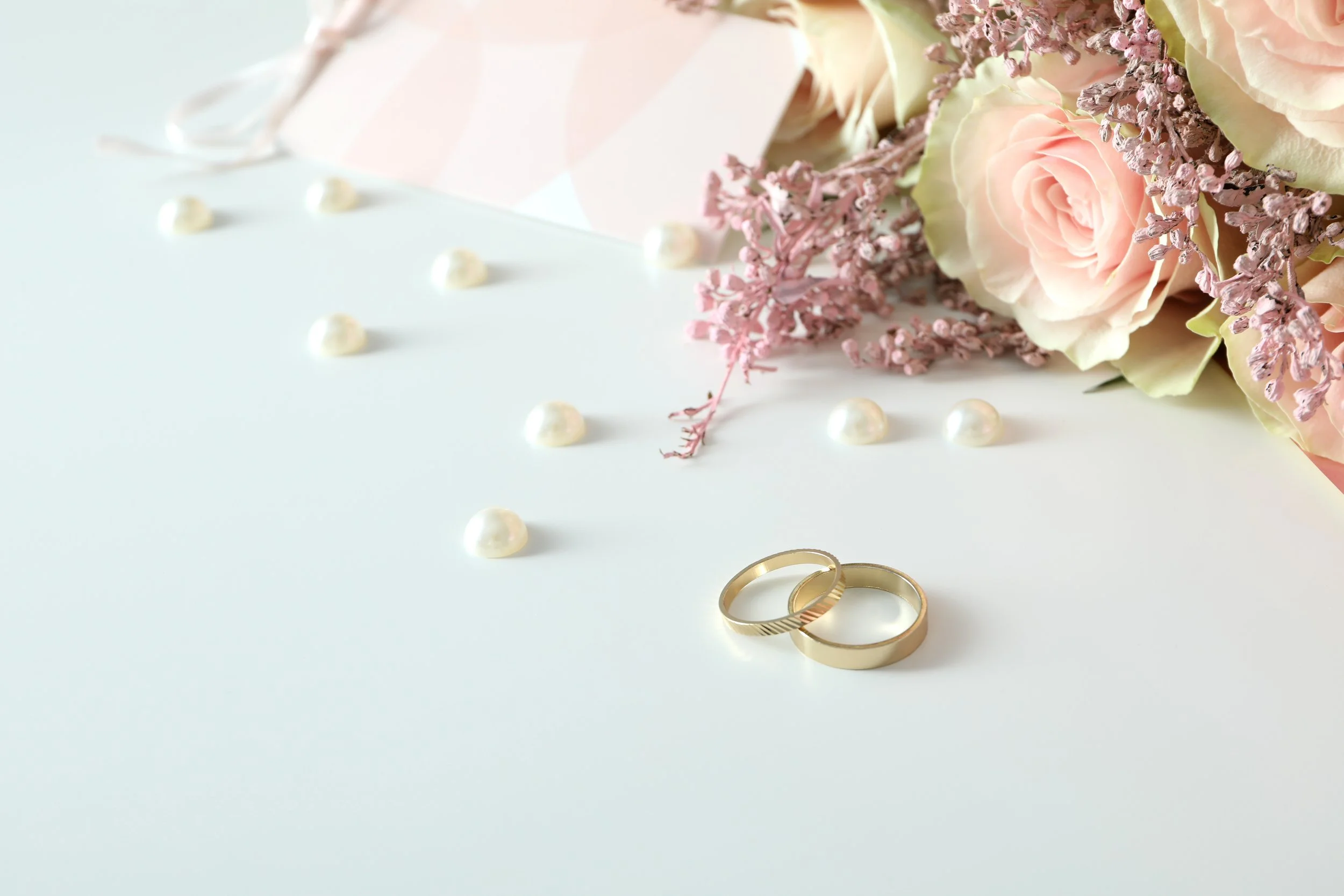 Un bouquet de roses pastel, des petites fleurs roses, des perles blanches, deux bagues en or
