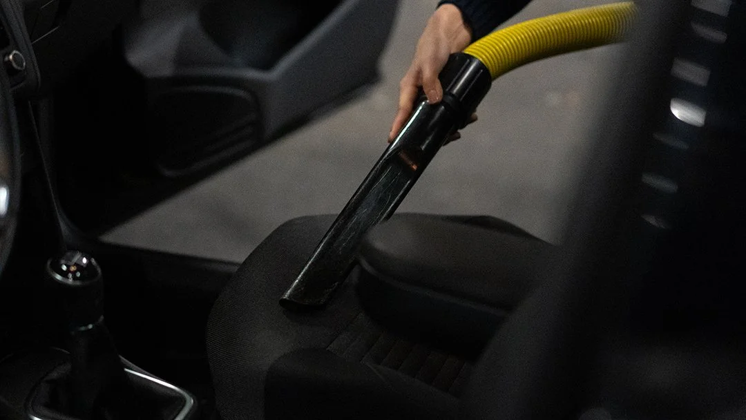 Eine Hand hält einen Staubsauger, der auf einem Autositz im Inneren eines Fahrzeugs verwendet wird.