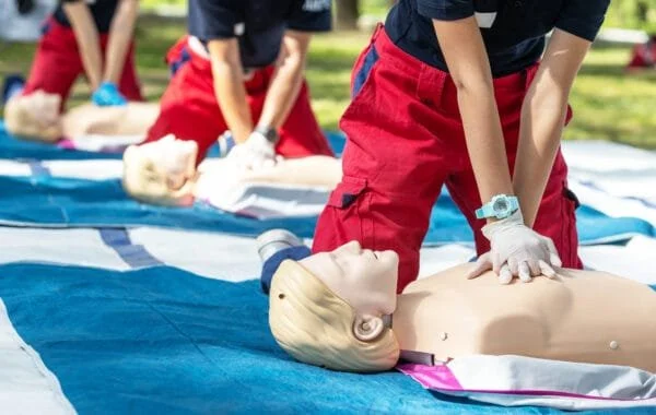Person practicing CPR on a mannequin during a training session outdoors.