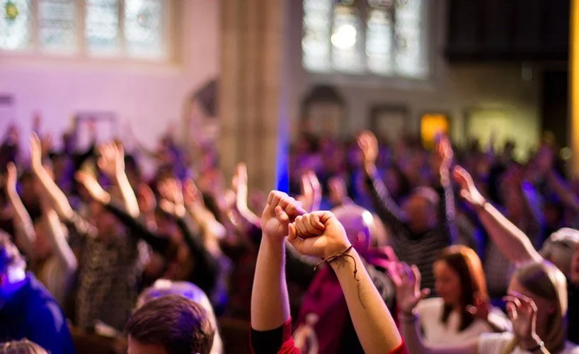 People in a large gathering raising their hands. Worship. Church. Church Safety.