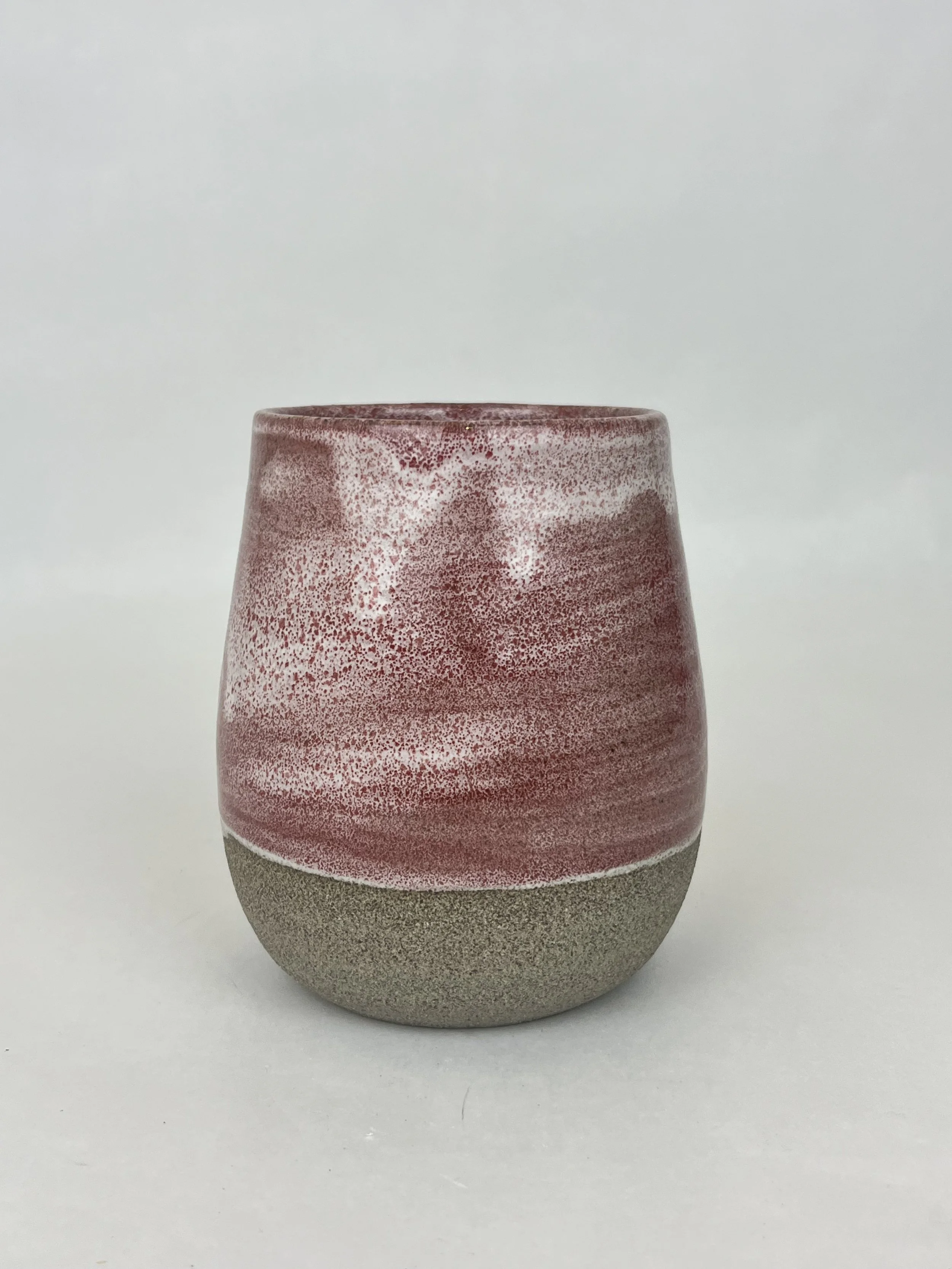 Eine zweifarbige Keramikvase mit einer rauen, grau-beigen unteren Hälfte und einer rot-weißen, spritzenden Oberseite.