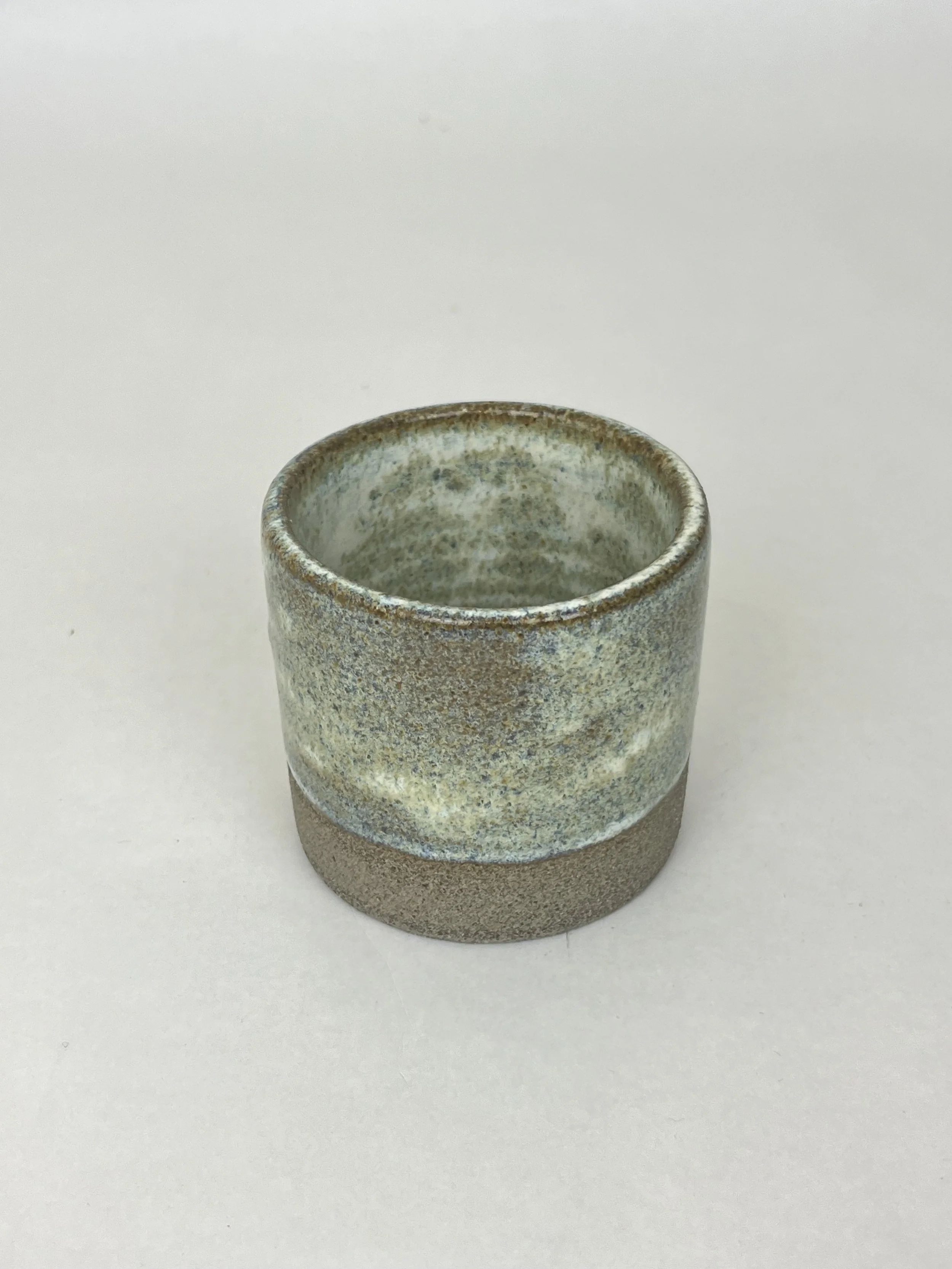 Kleine runde Keramikvase mit rauer Oberfläche, halb transparent mit grauen, weißen und braunen Farbtönen, steht auf einem weißen Hintergrund.