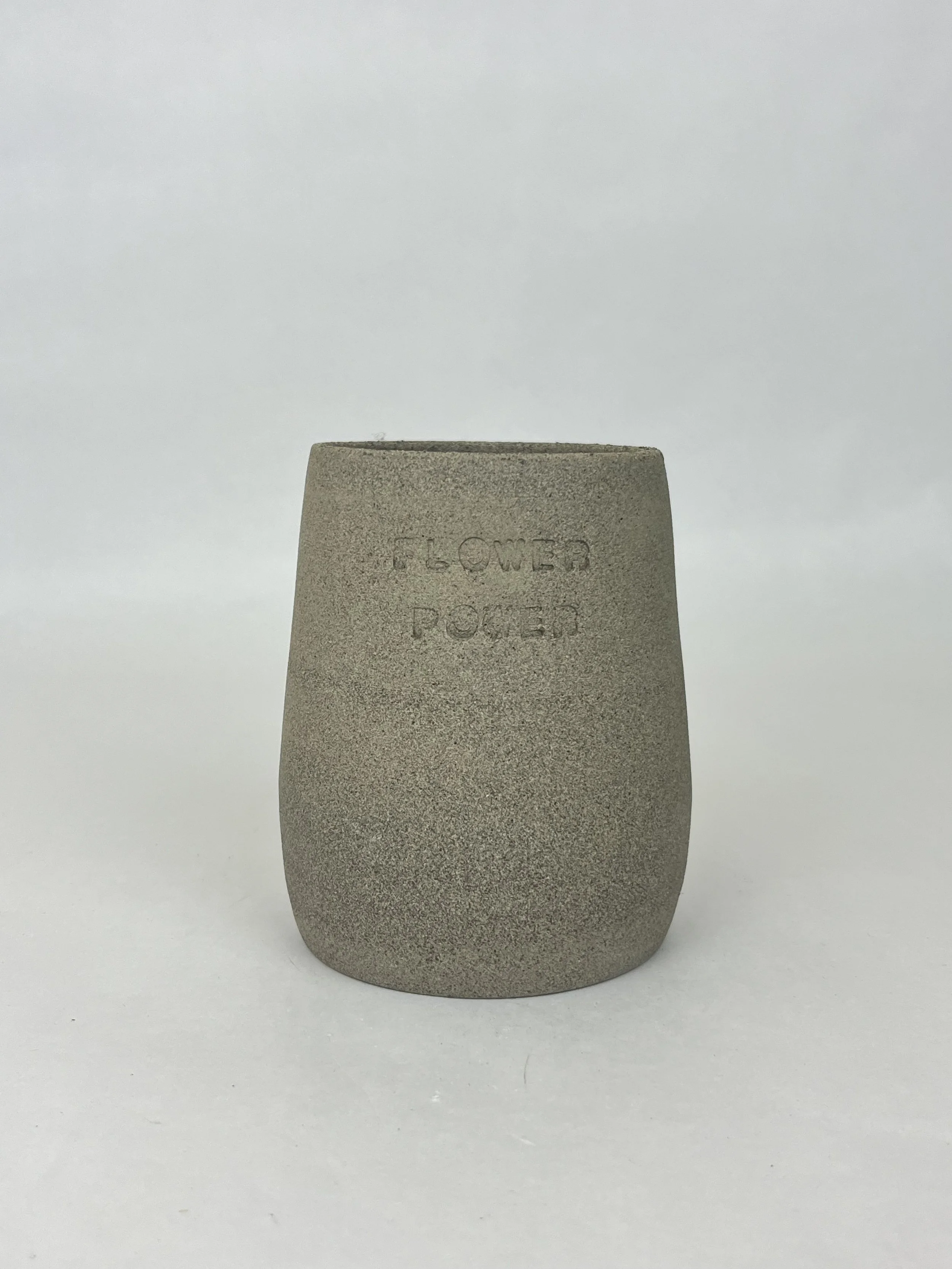 Ein grauer Keramikbecher mit der Aufschrift »FLOWER POKER« auf der Vorderseite, vor einem weißen Hintergrund.