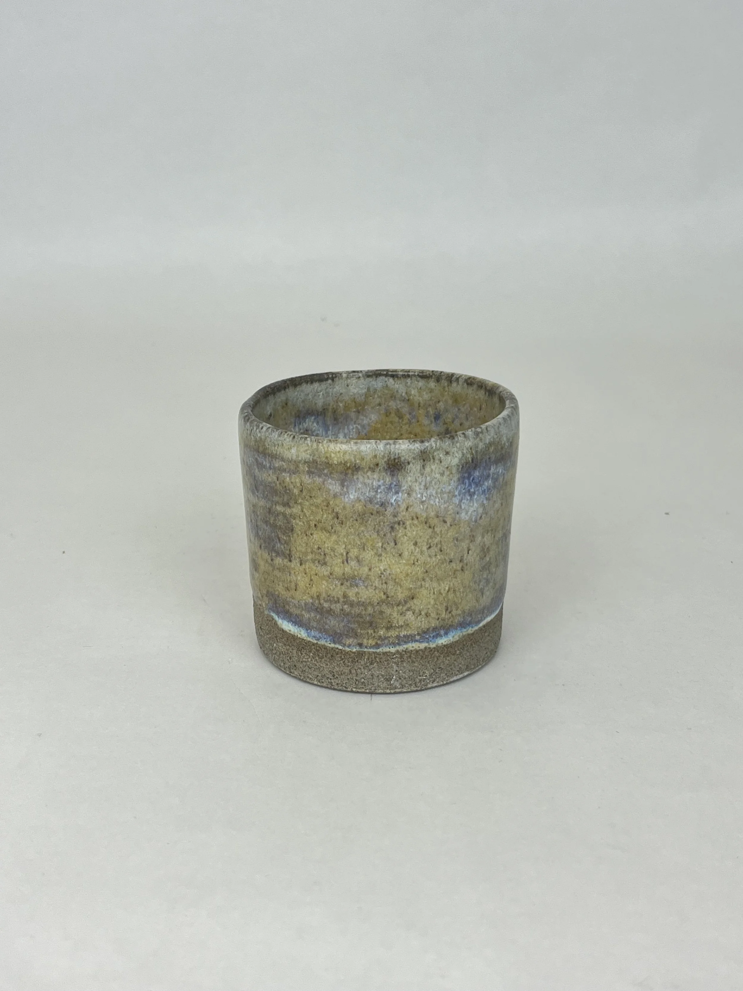 Kleine Vase mit erdigen Farben und blauen Akzenten auf weißem Hintergrund