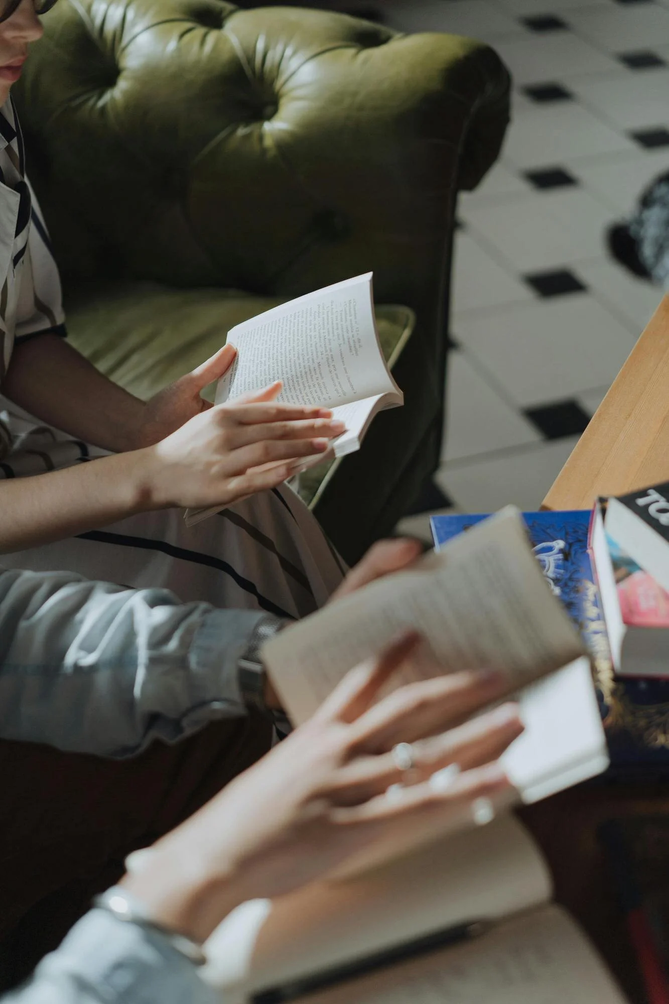 group of people thumbing through the pages of books sitting on a couch next to coffee table with piles of books
