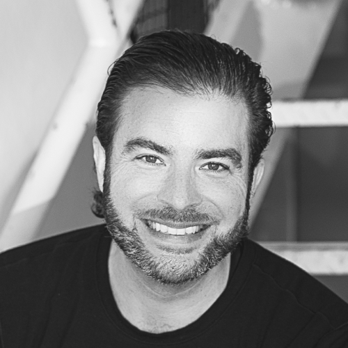 Black-and-white portrait of a smiling man with slicked-back hair and a beard.