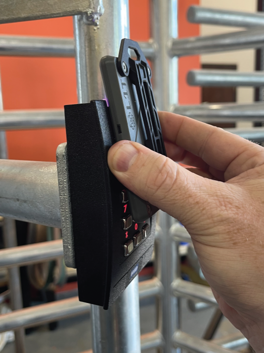 Person holding a multi-tool or device against a metal scaffolding structure in a gym or construction area.