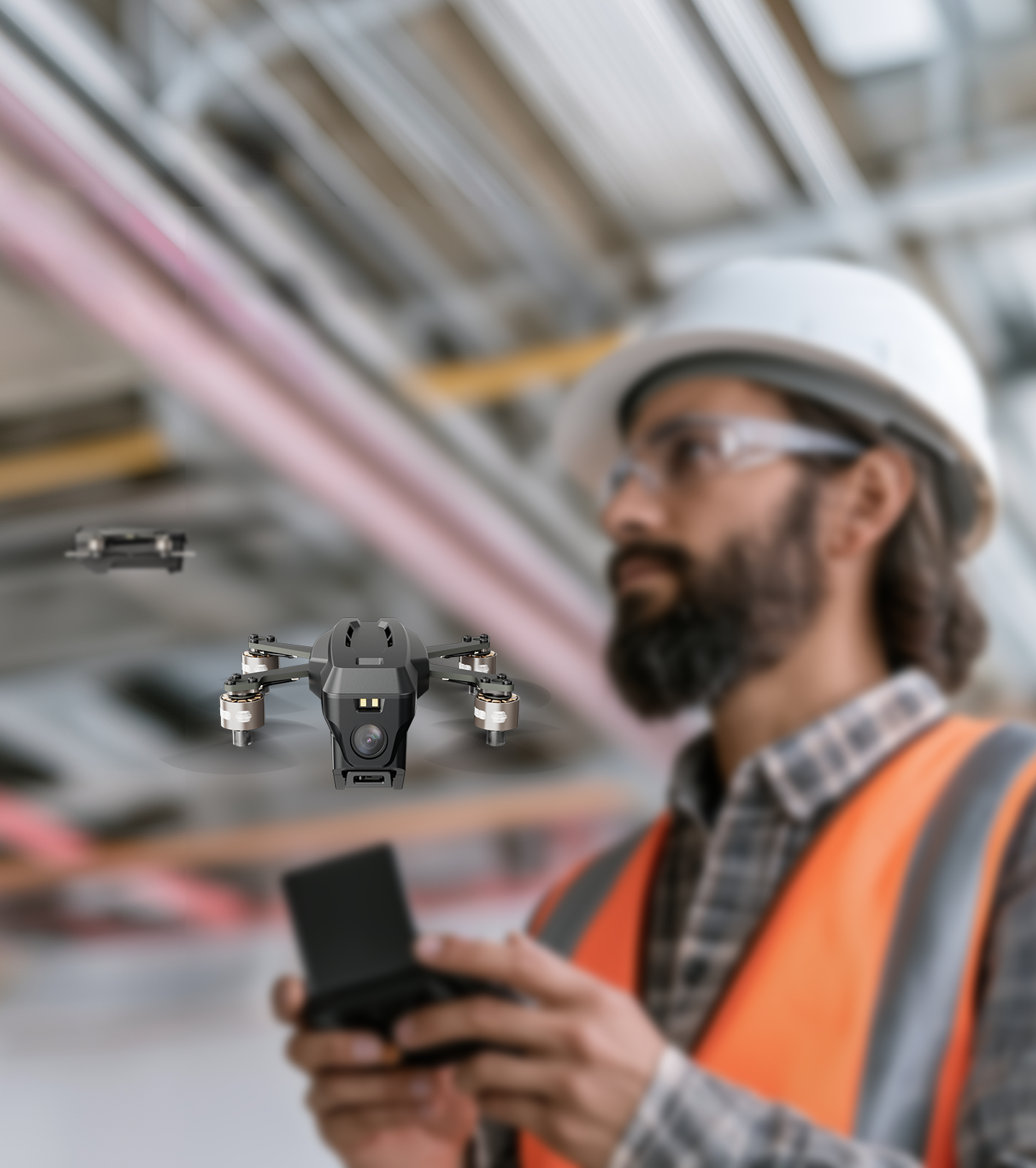 A man wearing a hard hat, safety glasses, and a high-visibility vest holding a remote control drone with a camera, in a warehouse or industrial setting.