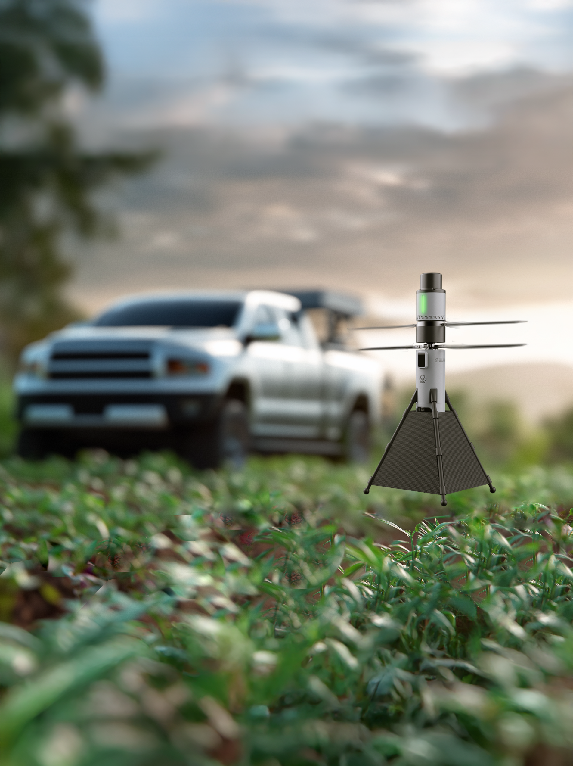 A drone flying over leafy ground with a blurred white vehicle and a wind turbine in the background during sunset.