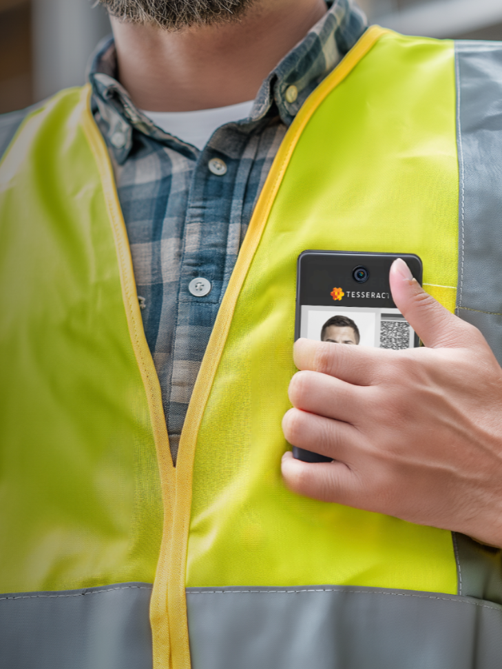 Person wearing a yellow safety vest, holding a smartphone with a digital ID or passport displayed on the screen.