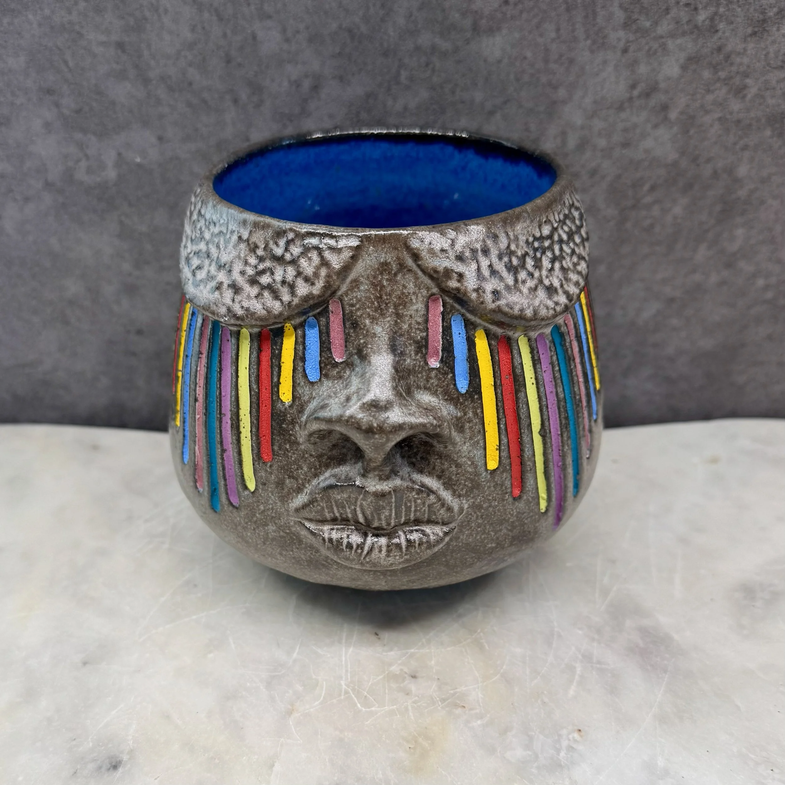 Close-up of a ceramic face with colorful vertical stripes and a textured surface.