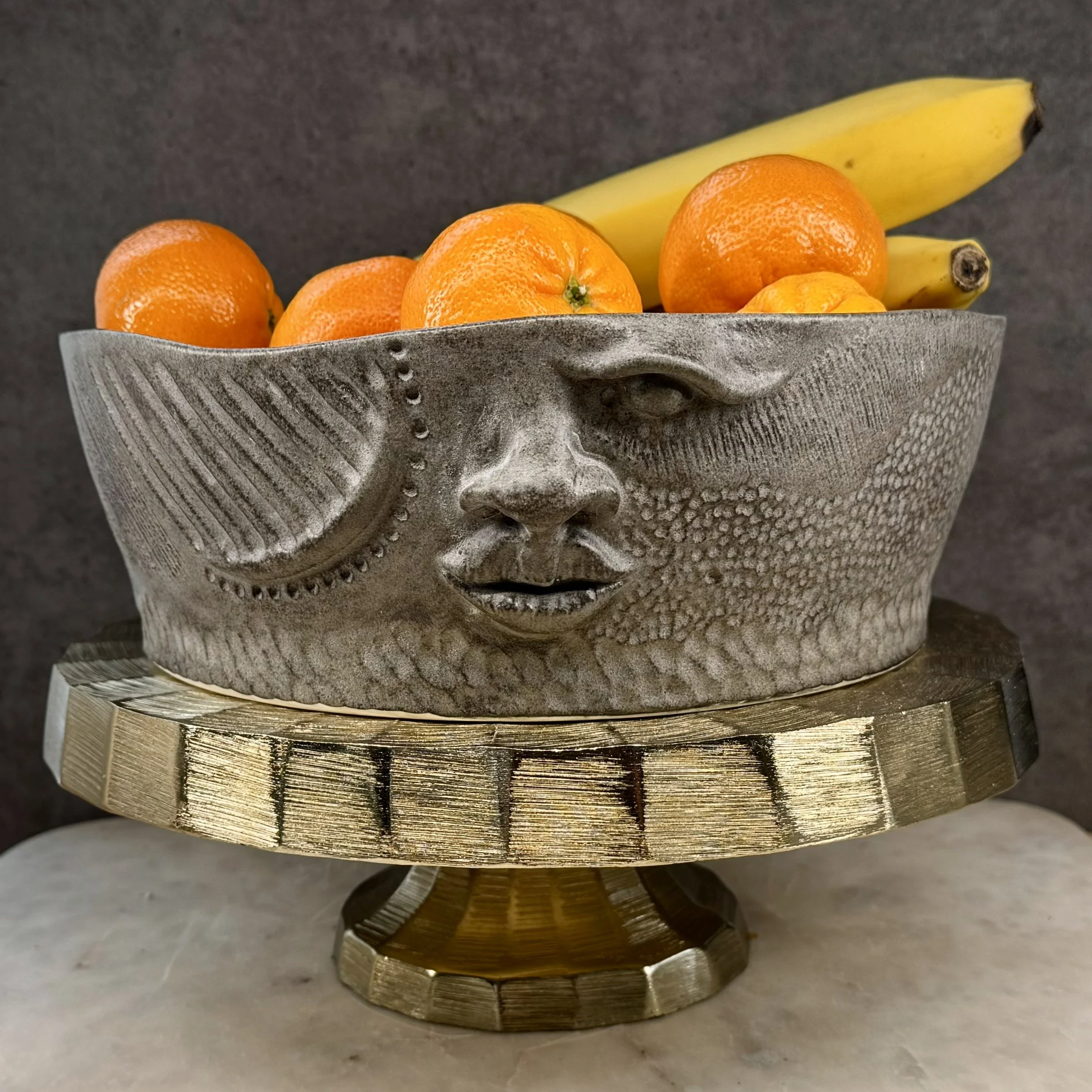 A decorative bowl shaped like a human face, filled with oranges and bananas.