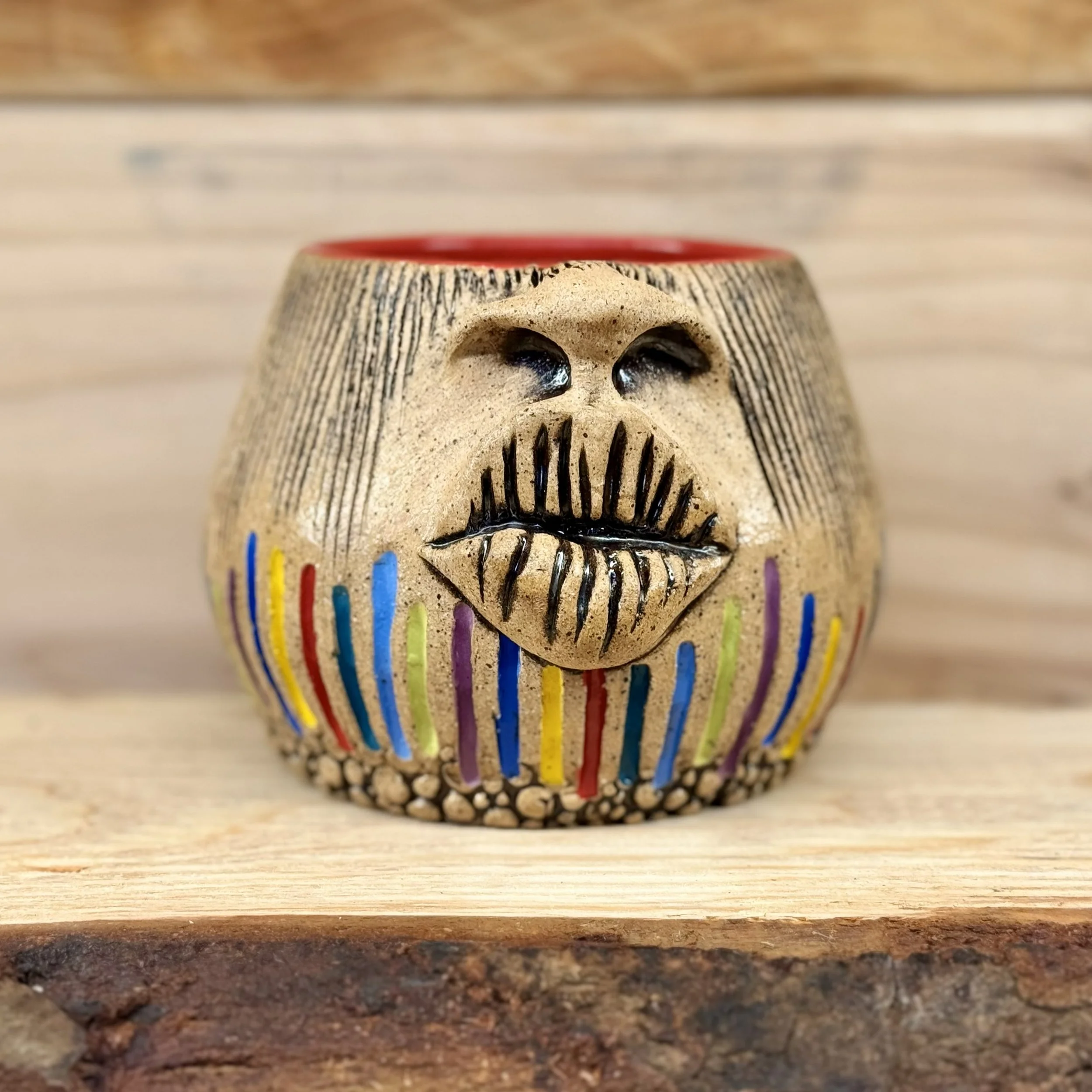Close-up image of a decorated skull-shaped ceramic container with colorful vertical lines, set on a wooden surface with a blurred background.