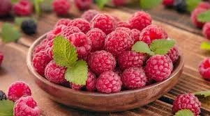 A bowl of fresh raspberries with a few mint leaves on top, placed on a wooden surface.