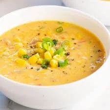Creamy yellow corn soup garnished with chopped green onions in a white bowl.