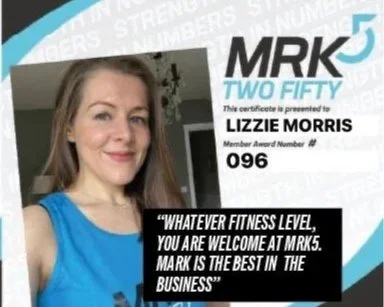 A woman holding a certification from MRK5 with the name Lizzie Morris, smiling for a selfie.
