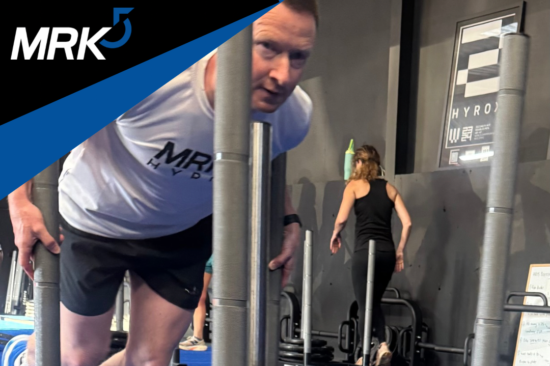 Man and woman working out in a gym, with the man in the foreground and the woman in the background, both using exercise equipment.