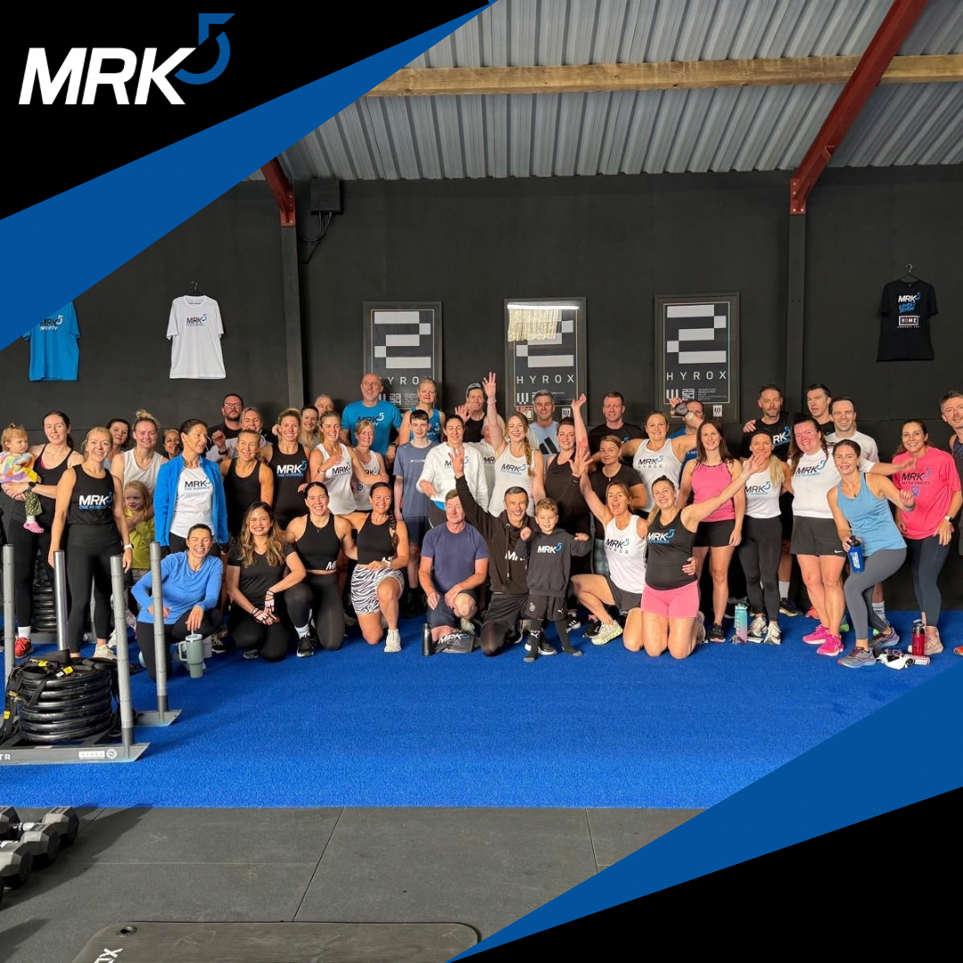 A large group of people in athletic wear inside a gym, posing for a group photo, some smiling and making peace signs.