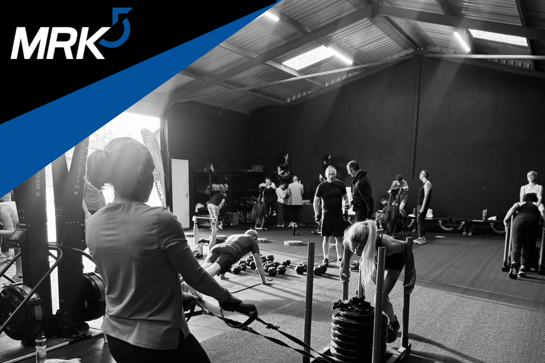 People working out at a gym with weights, resistance bands, and exercise equipment, in a spacious indoor fitness area.