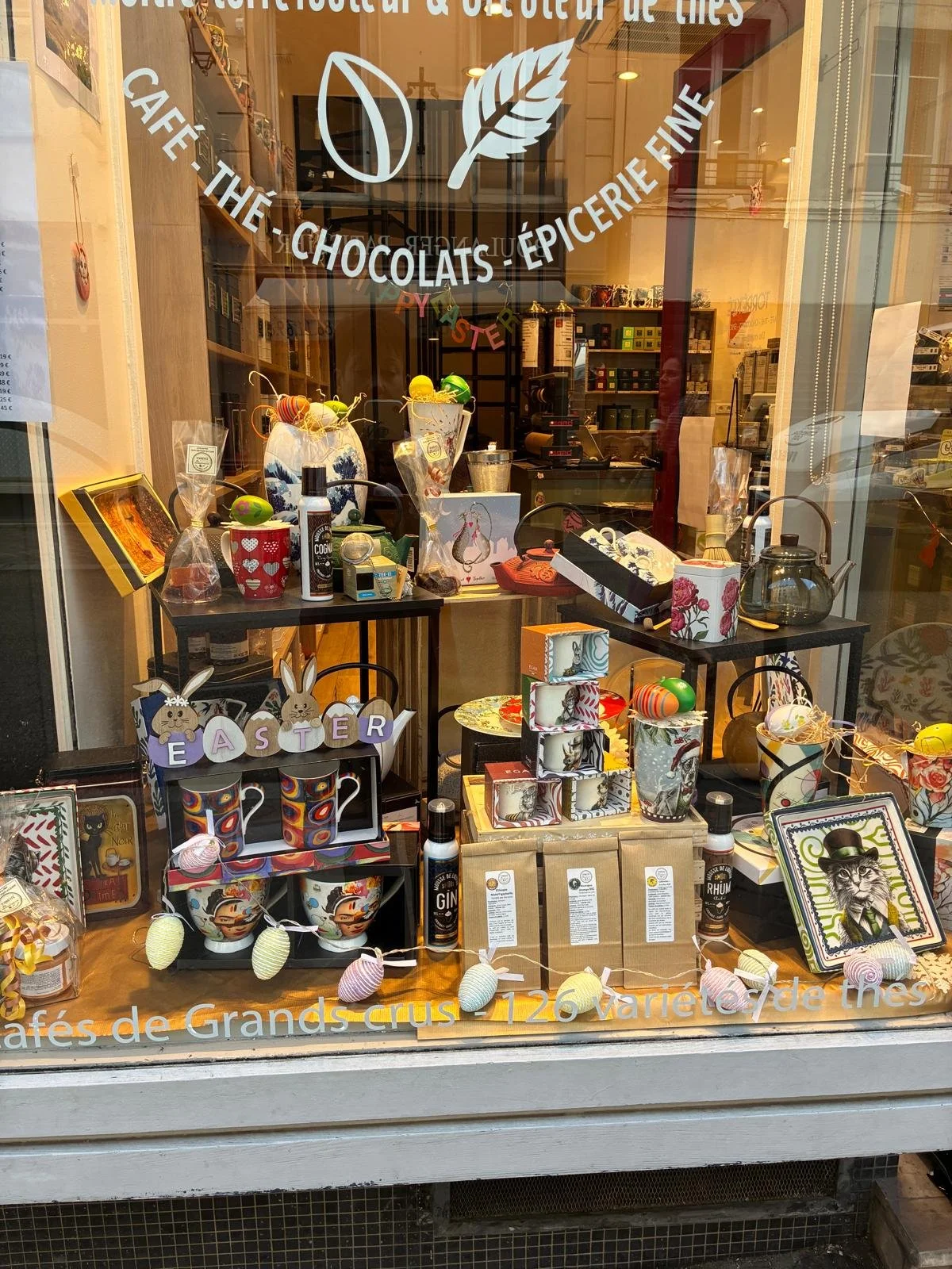 Vitrine d'une boutique proposant des chocolats, thé, épicerie fine, cadeaux de Pâques, accessoires et produits divers avec une décoration printanière.