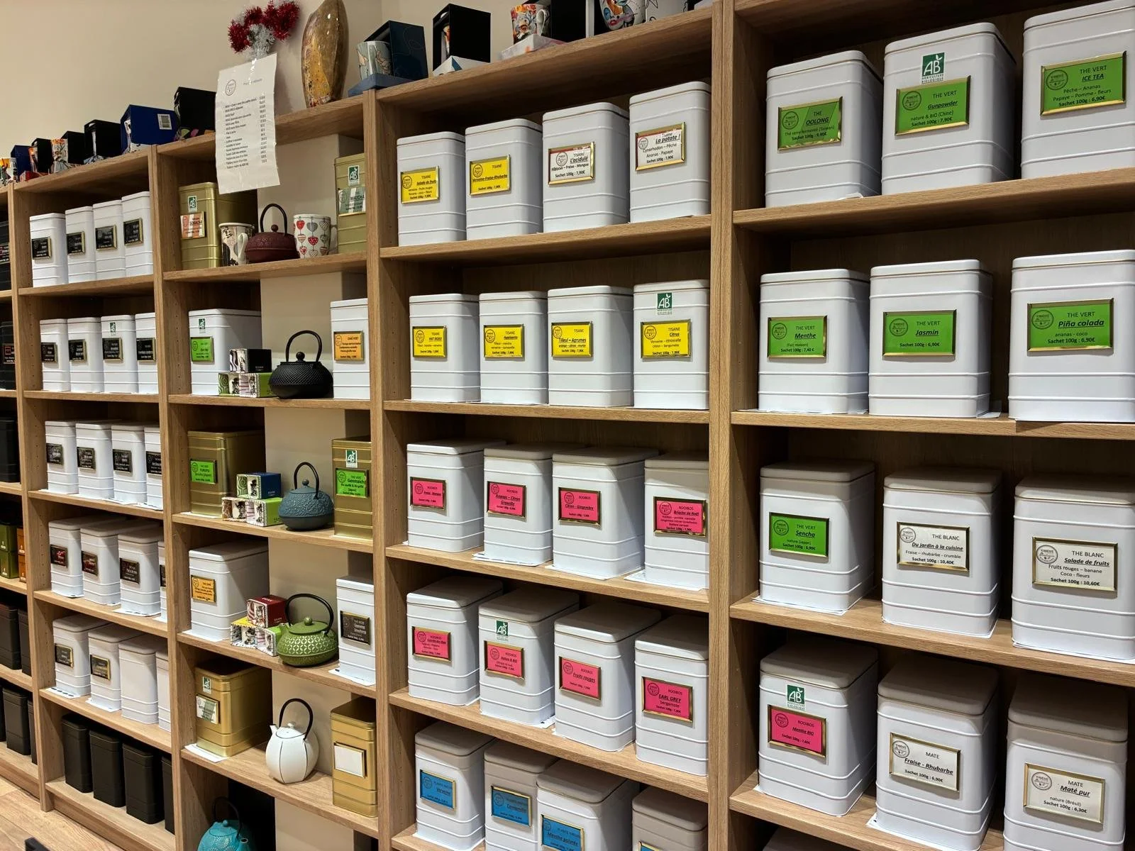 Étagères en bois remplies de boîtes de thé de différentes couleurs avec étiquettes colorées, dans un magasin.