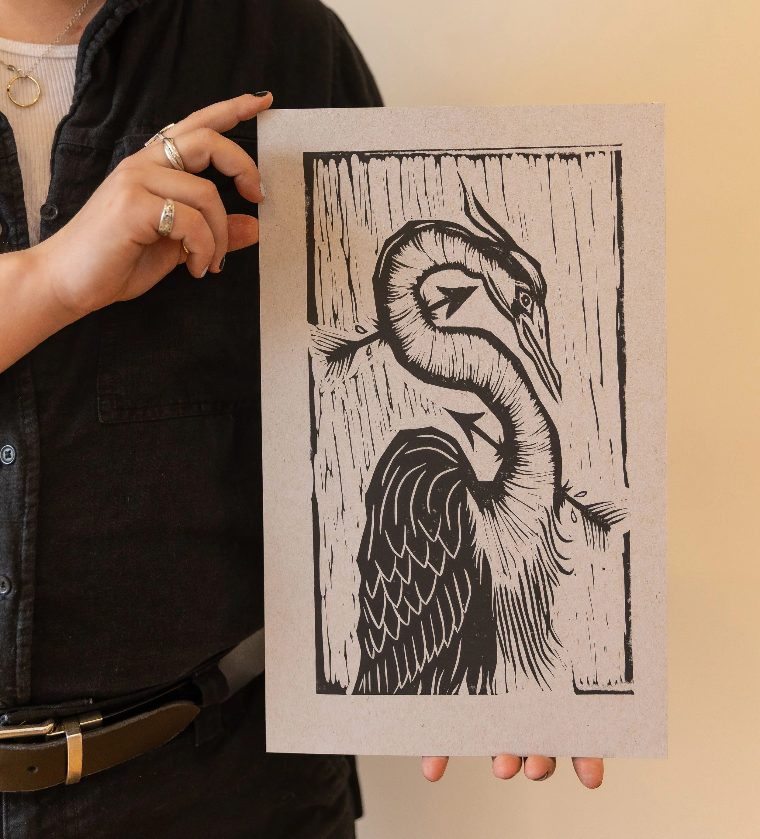 Black and white linleum print of a heron, being pierced by two arrows. It has carved details in the feathers and neck.