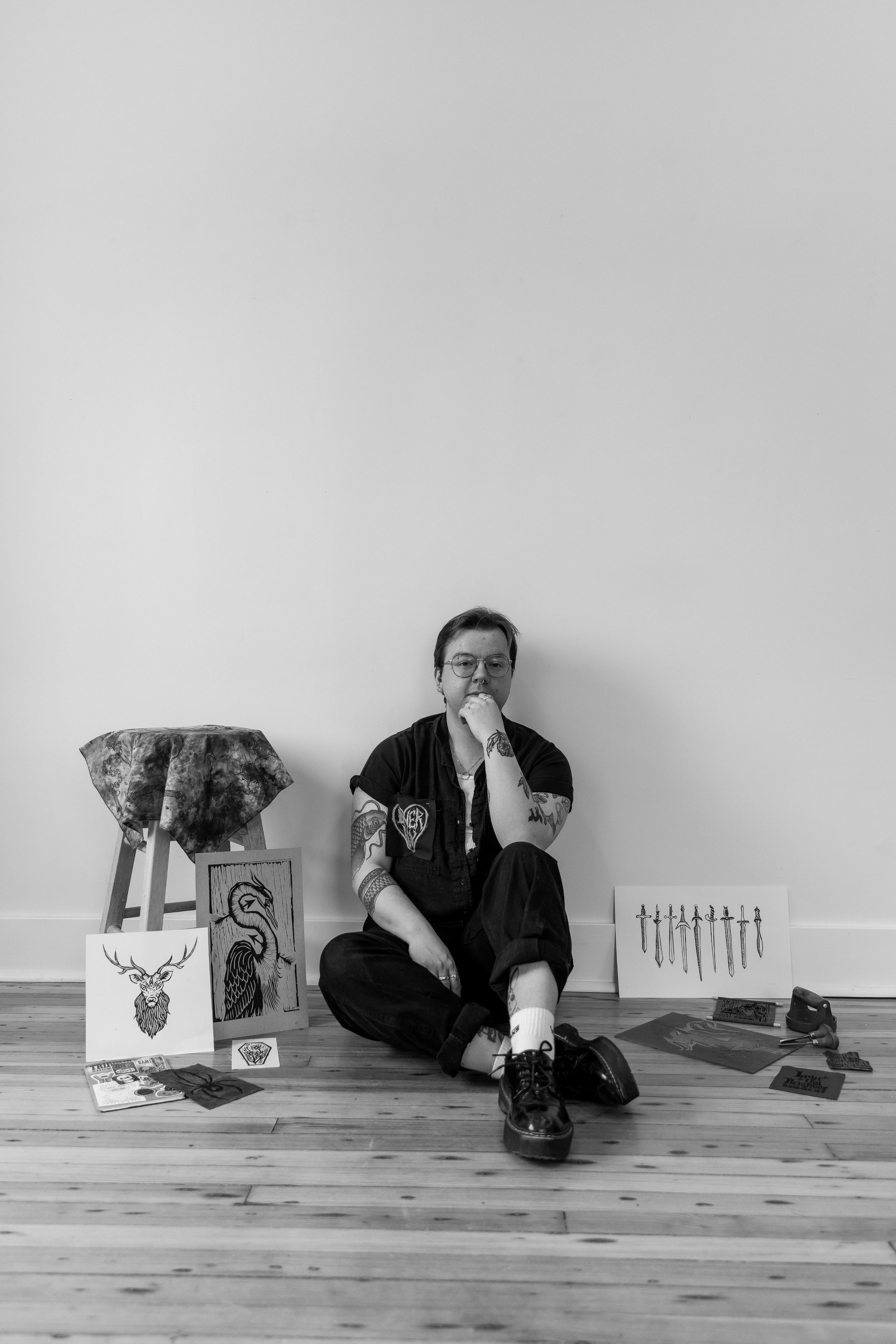 Black and white photo of Finnegan West sitting on the floor surrounded by artwork and items.