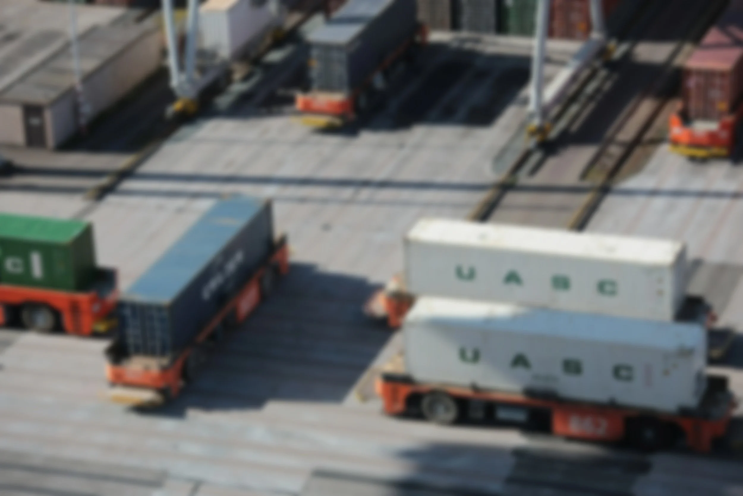 Blurry aerial view of freight trucks and containers at a shipping port or warehouse.