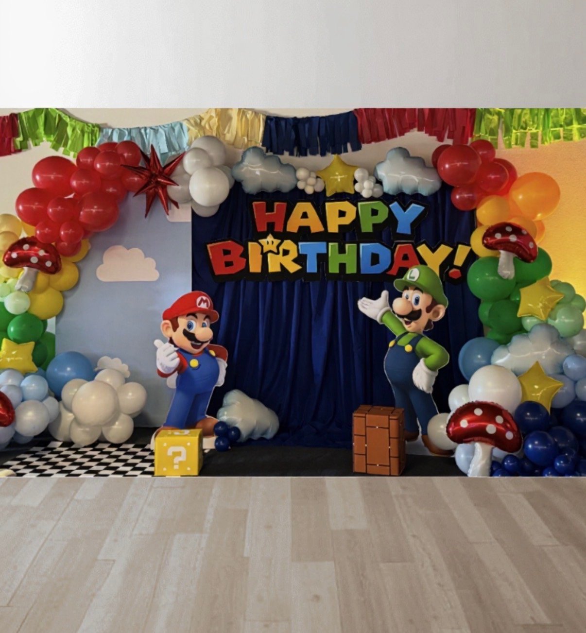 Colorful birthday party decoration with balloons, clouds, stars, mushrooms, and characters of Mario and Luigi from Nintendo, with a