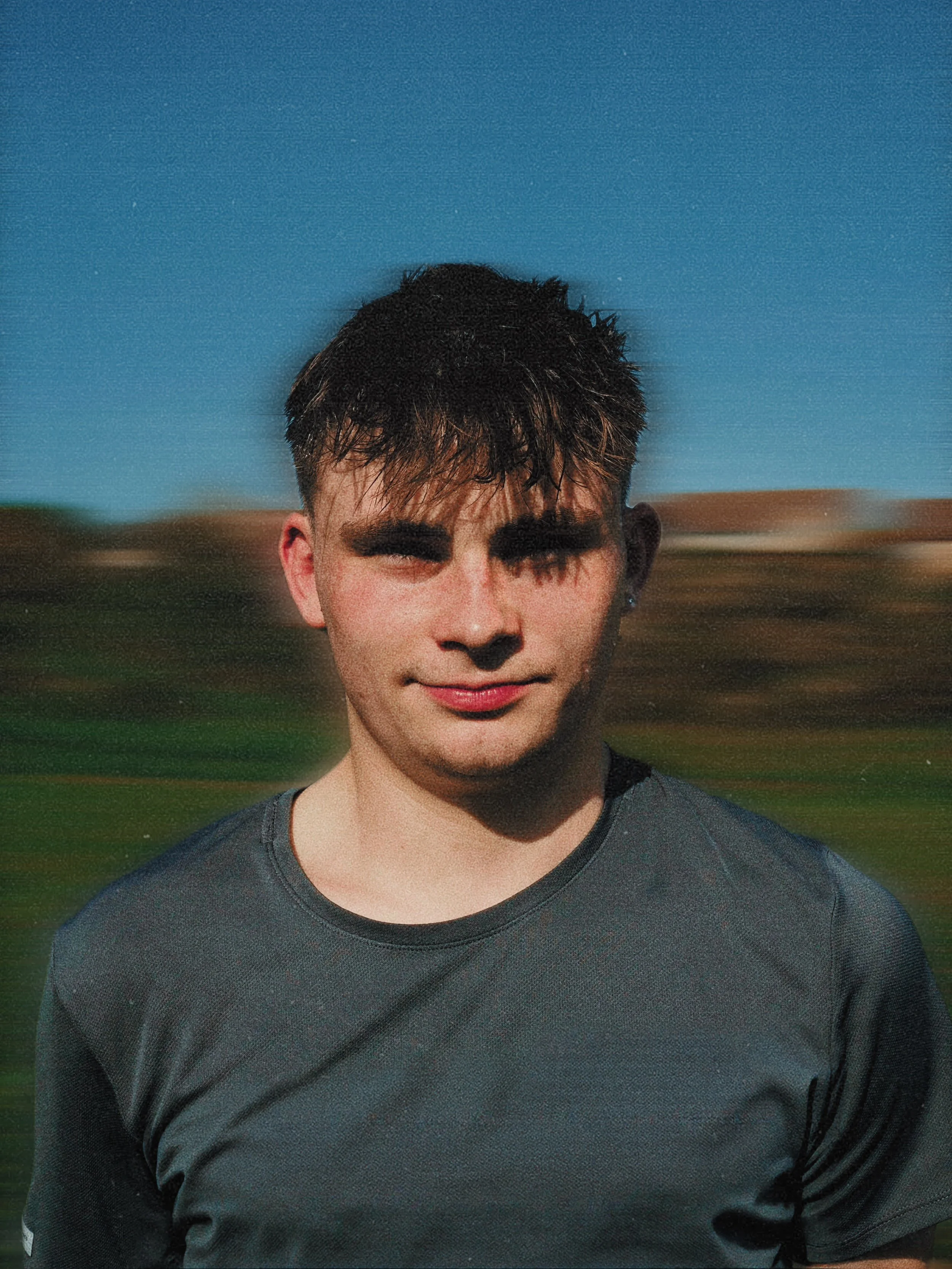 A young man with dark hair smiling outdoors on a sunny day.