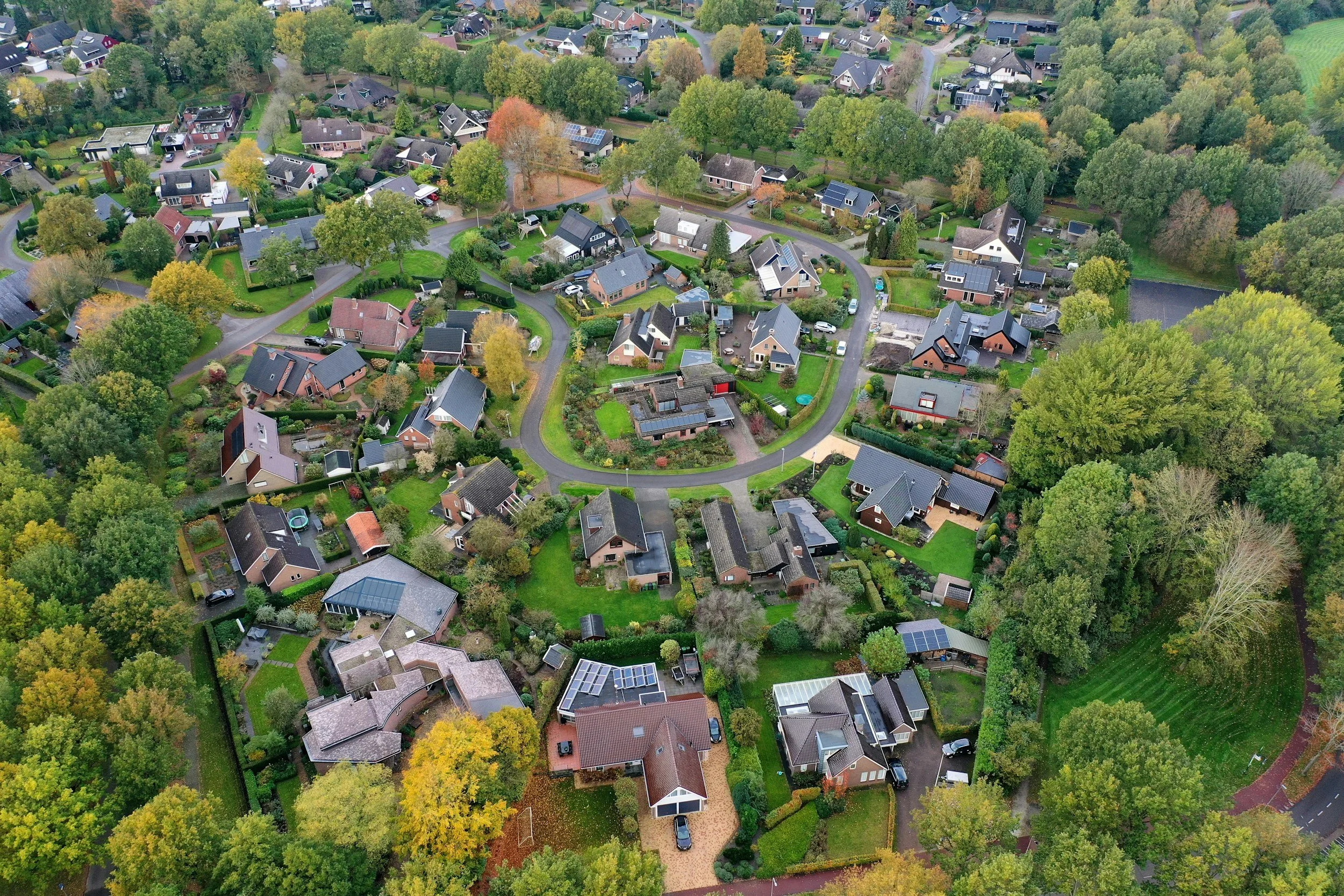 An aerial view of a suburban neighborhood with numerous houses, green trees, and winding roads.