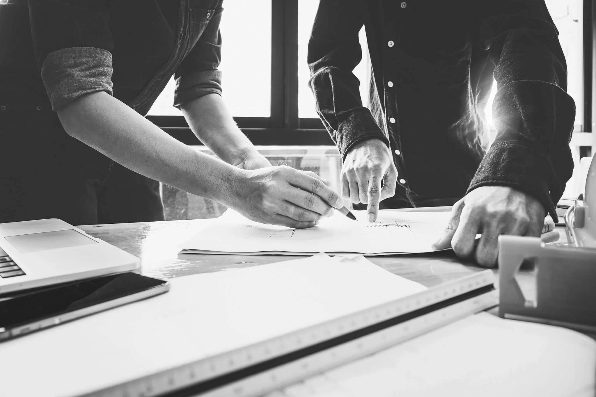 Two people working together at a desk, analyzing documents with a pen, with a window in the background
