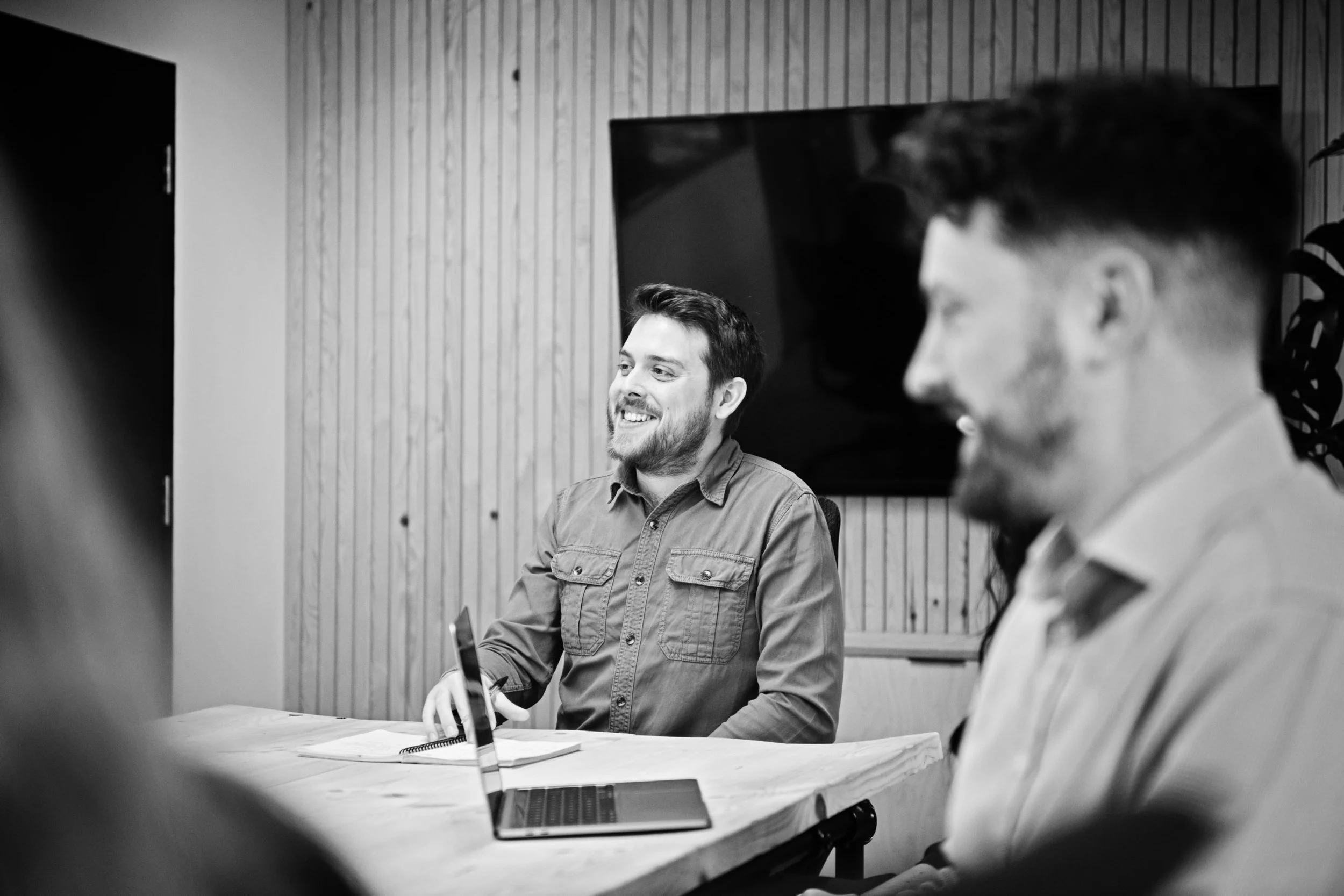 Two men sitting at a table in a meeting room, having a discussion.