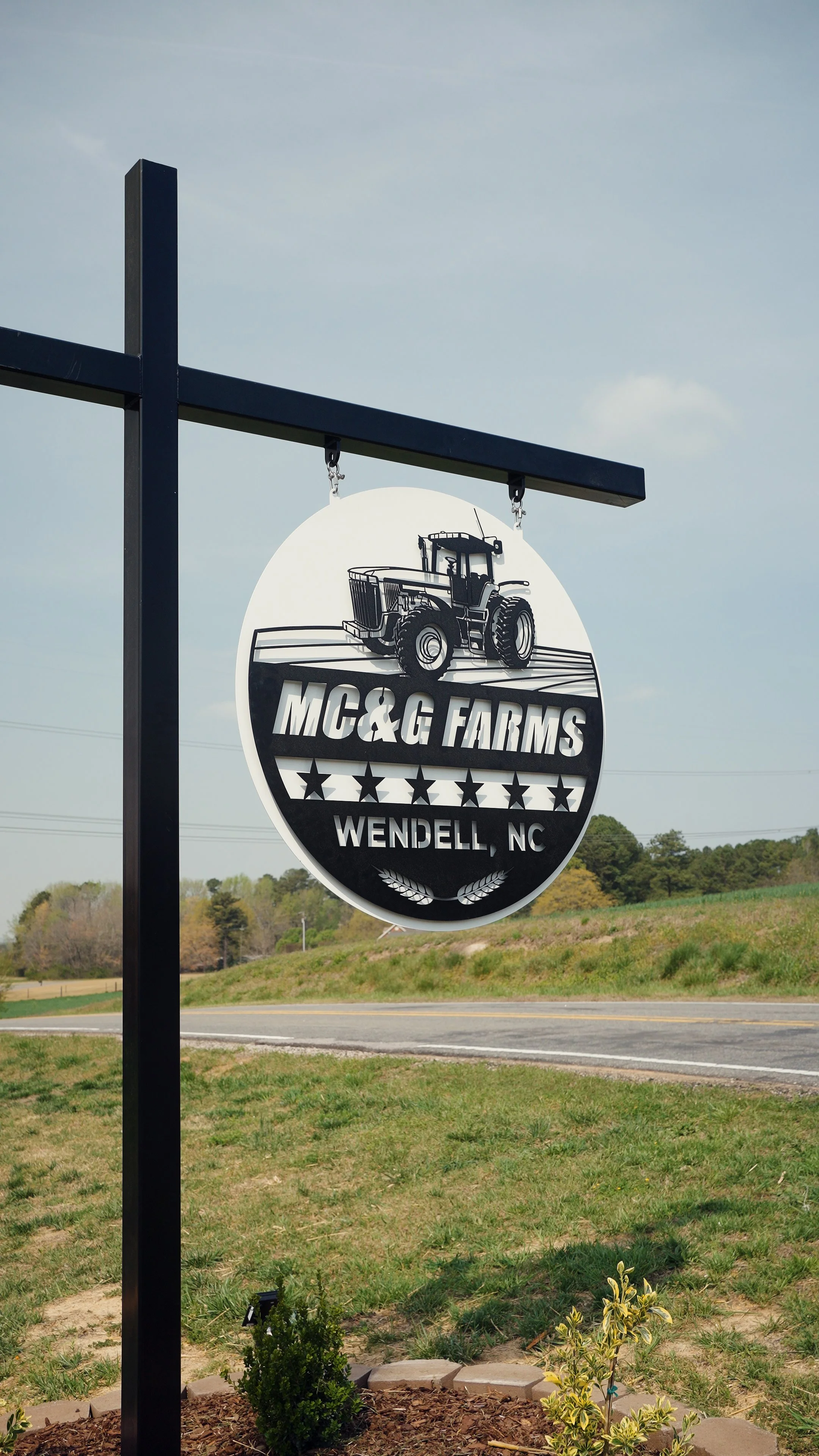 Sign for MC & G Farms in Wendell, North Carolina, featuring a tractor graphic, stars, and decorative wheat.