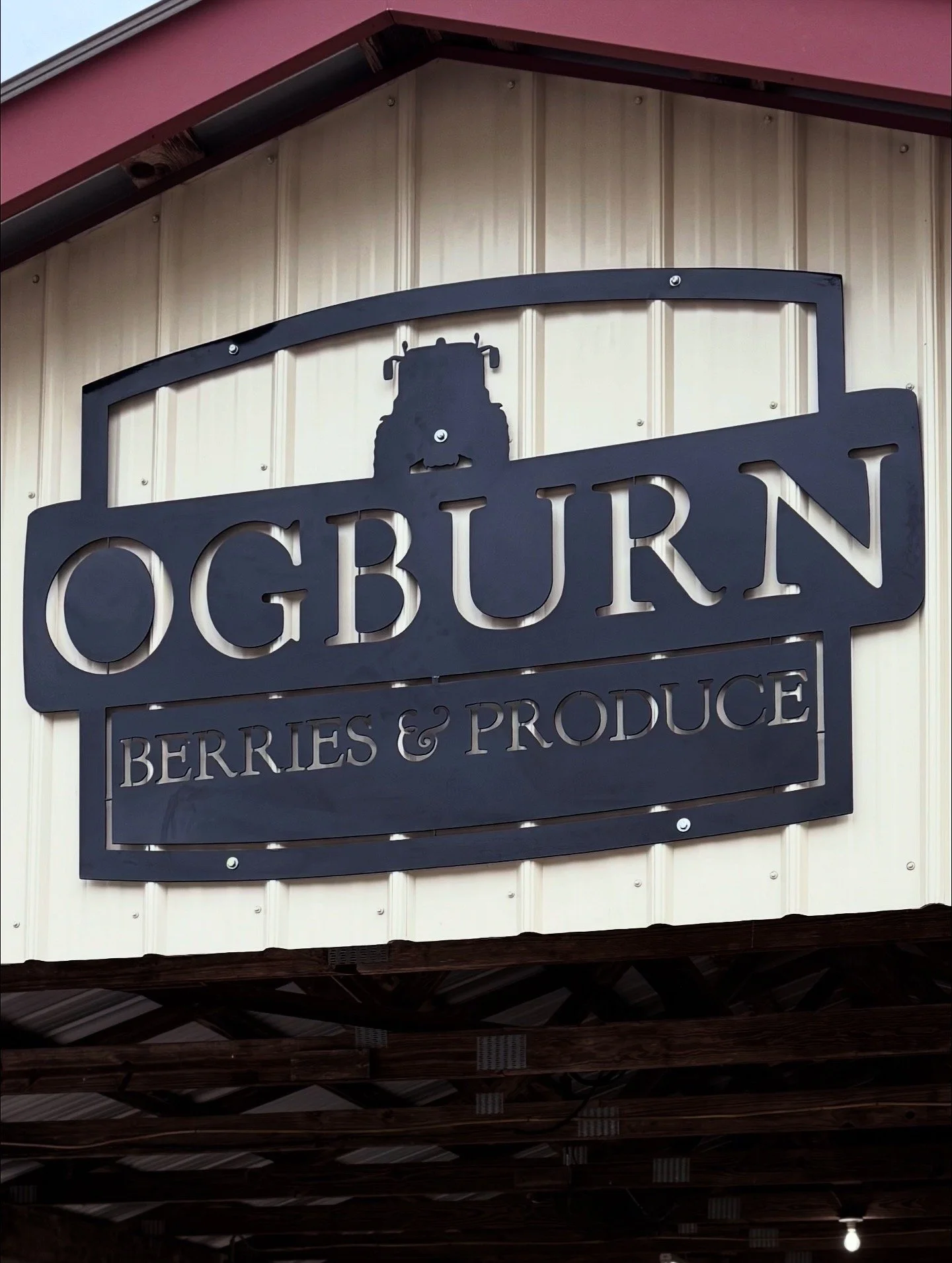 Sign for Ogburn Berries & Produce with a tractor silhouette above the text, mounted on the exterior wall of a building.