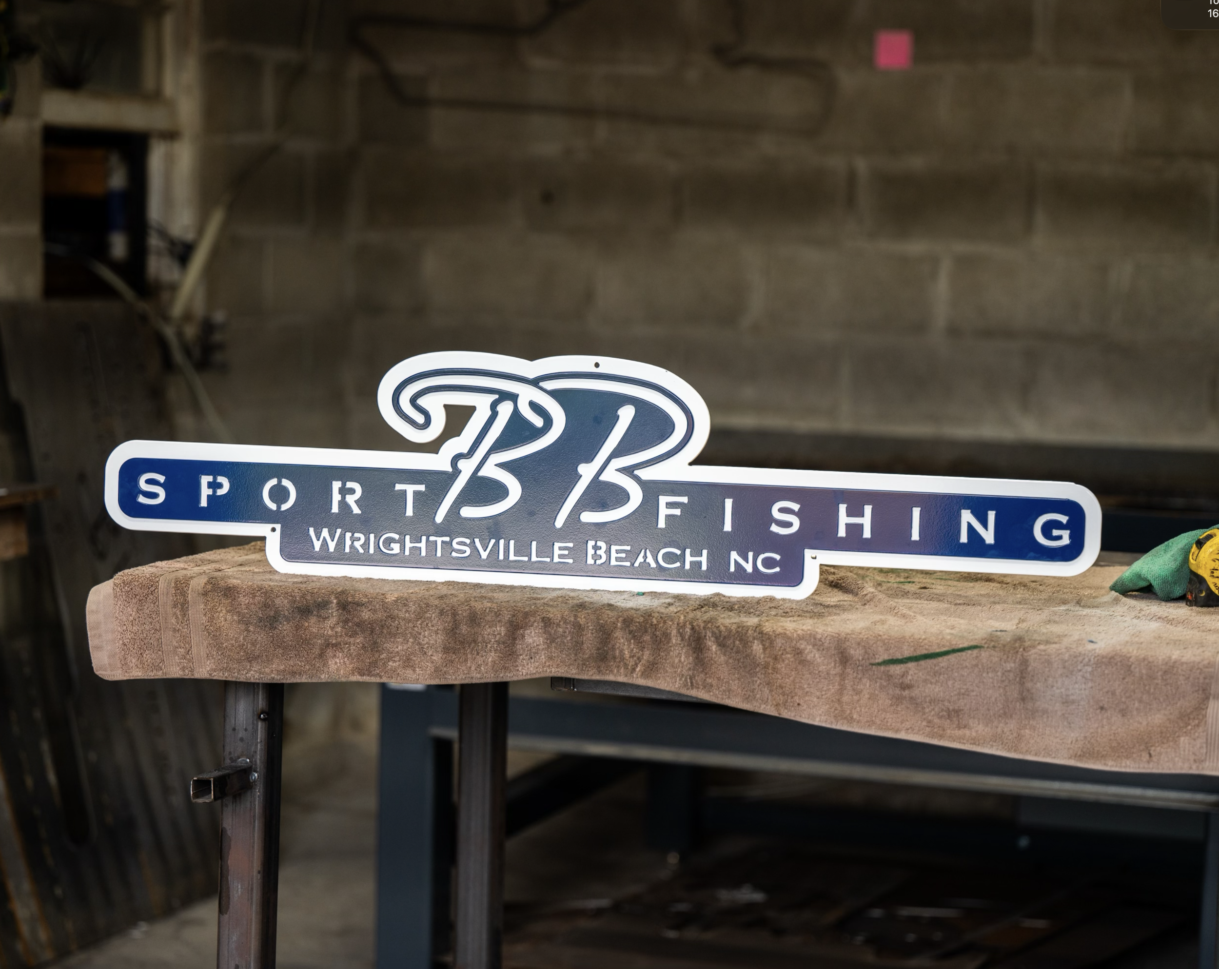 A sign that reads '33 Sport Fishing Wrightsville Beach NC' placed on a workbench in a workshop.