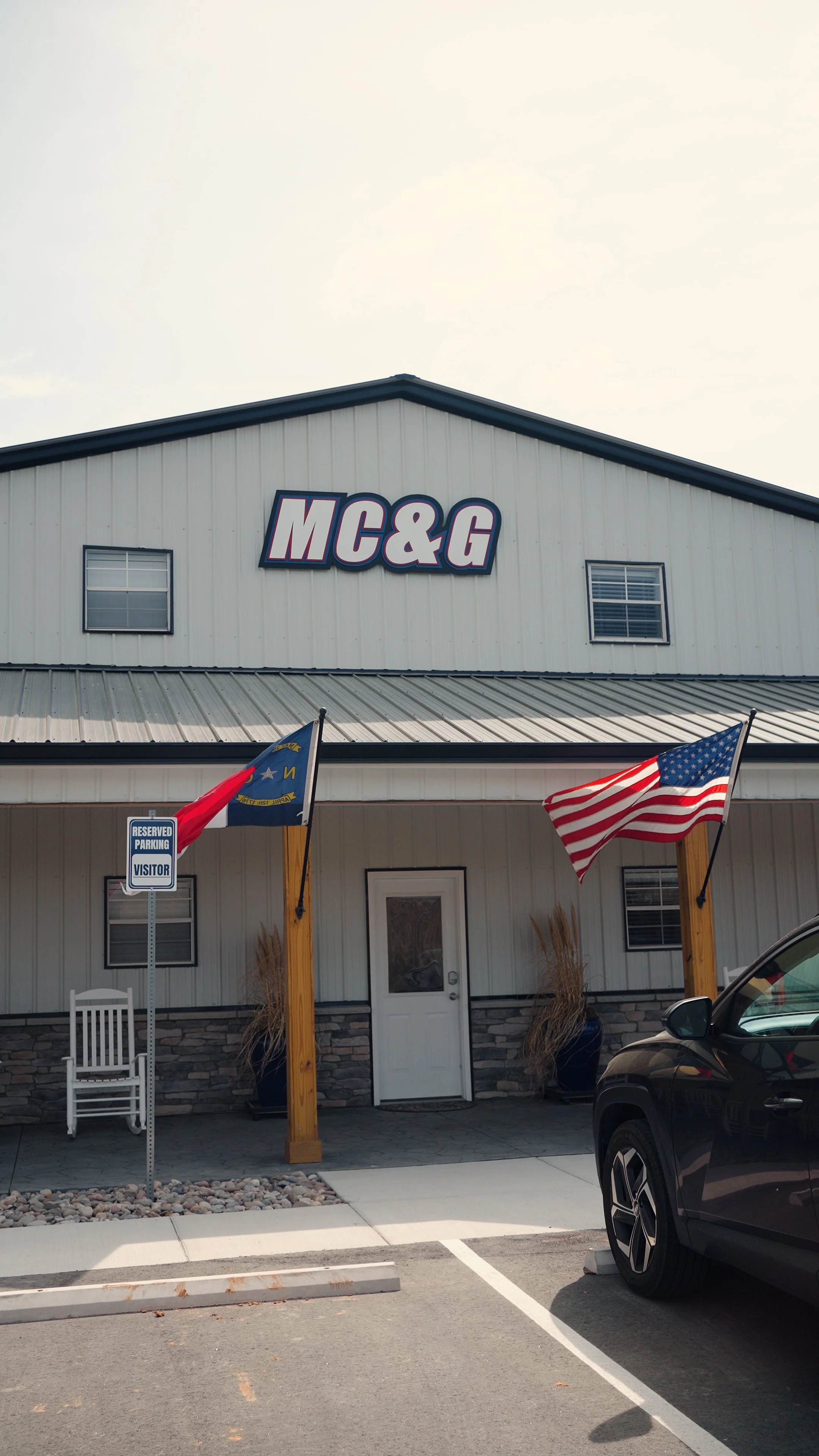 Front of a building with a sign that reads 'MC&G', flags of the United States and North Carolina, and a reserved parking sign.