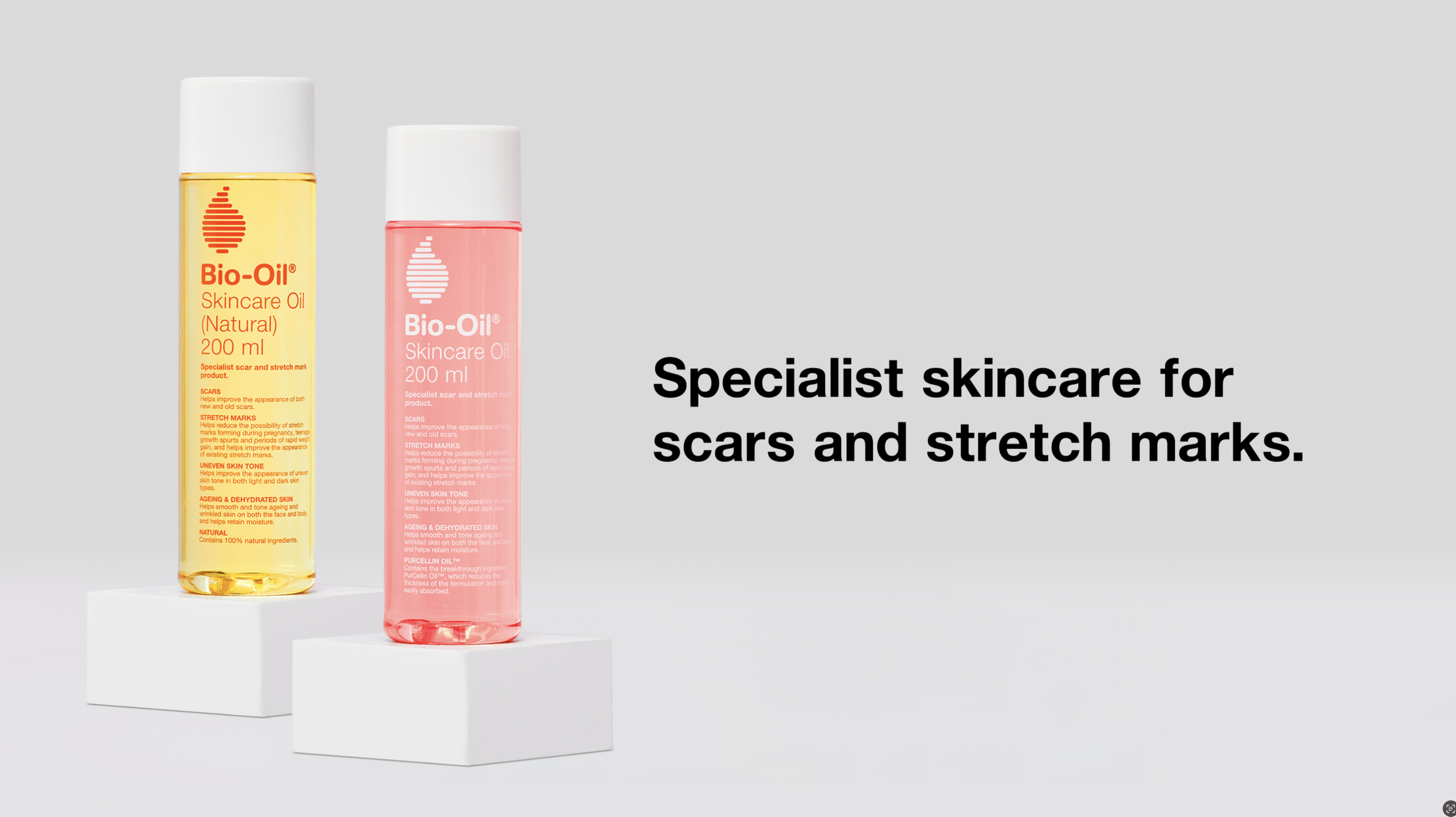 Two bottles of Bio-Oil skincare oil, one yellow and one pink, on white pedestals, with black text on a light background stating "Specialist skincare for scars and stretch marks."