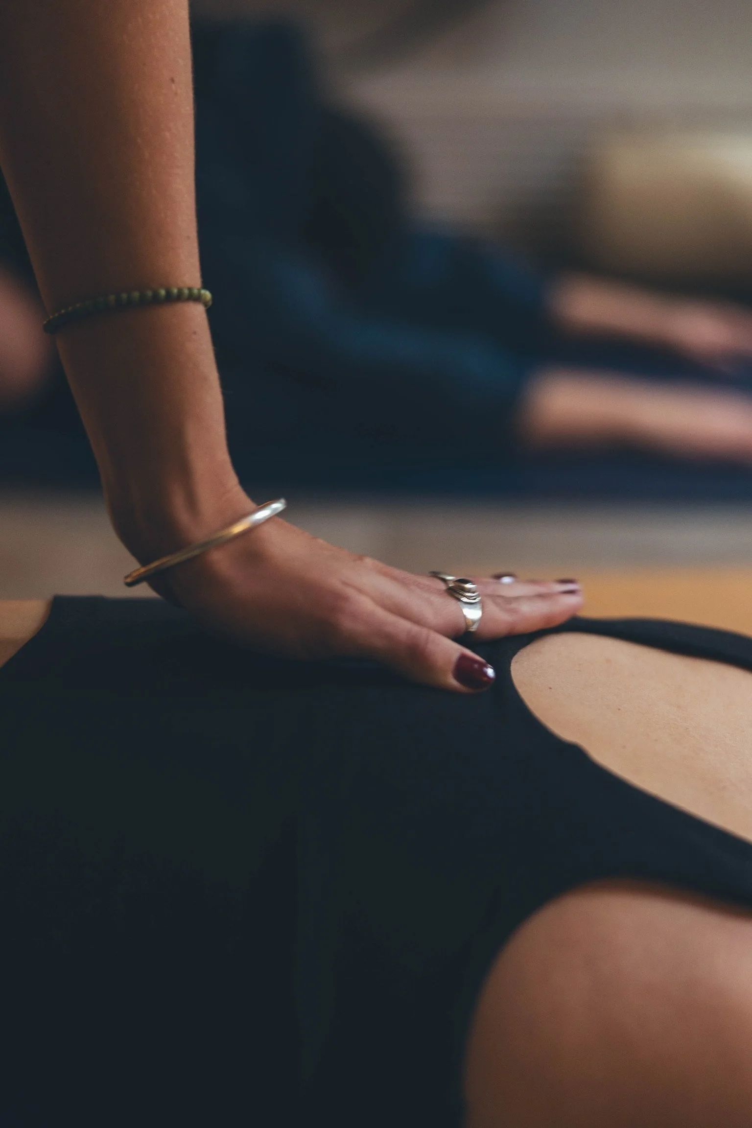 A person performing a yoga pose on a black mat, with their hand pressed against another person's back, in an indoor setting. Private Yoga session in their accomodation in Banff, Canmore.