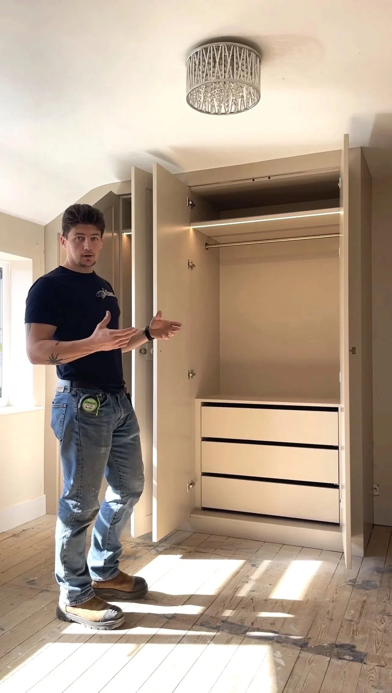 A man standing next to an open wardrobe in a room with wooden floors and a ceiling light.