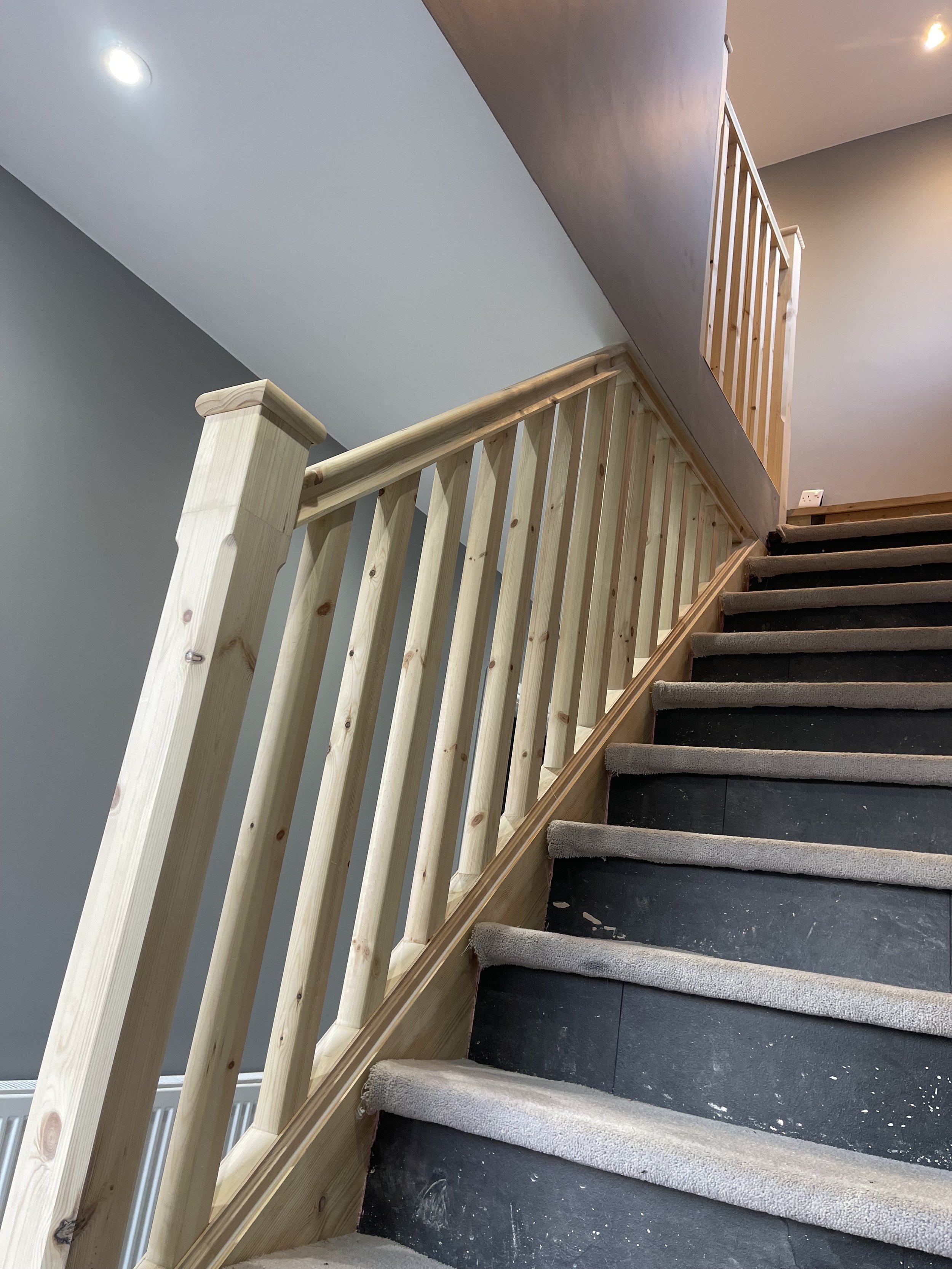 Interior staircase with wooden railing and carpeted steps under construction.