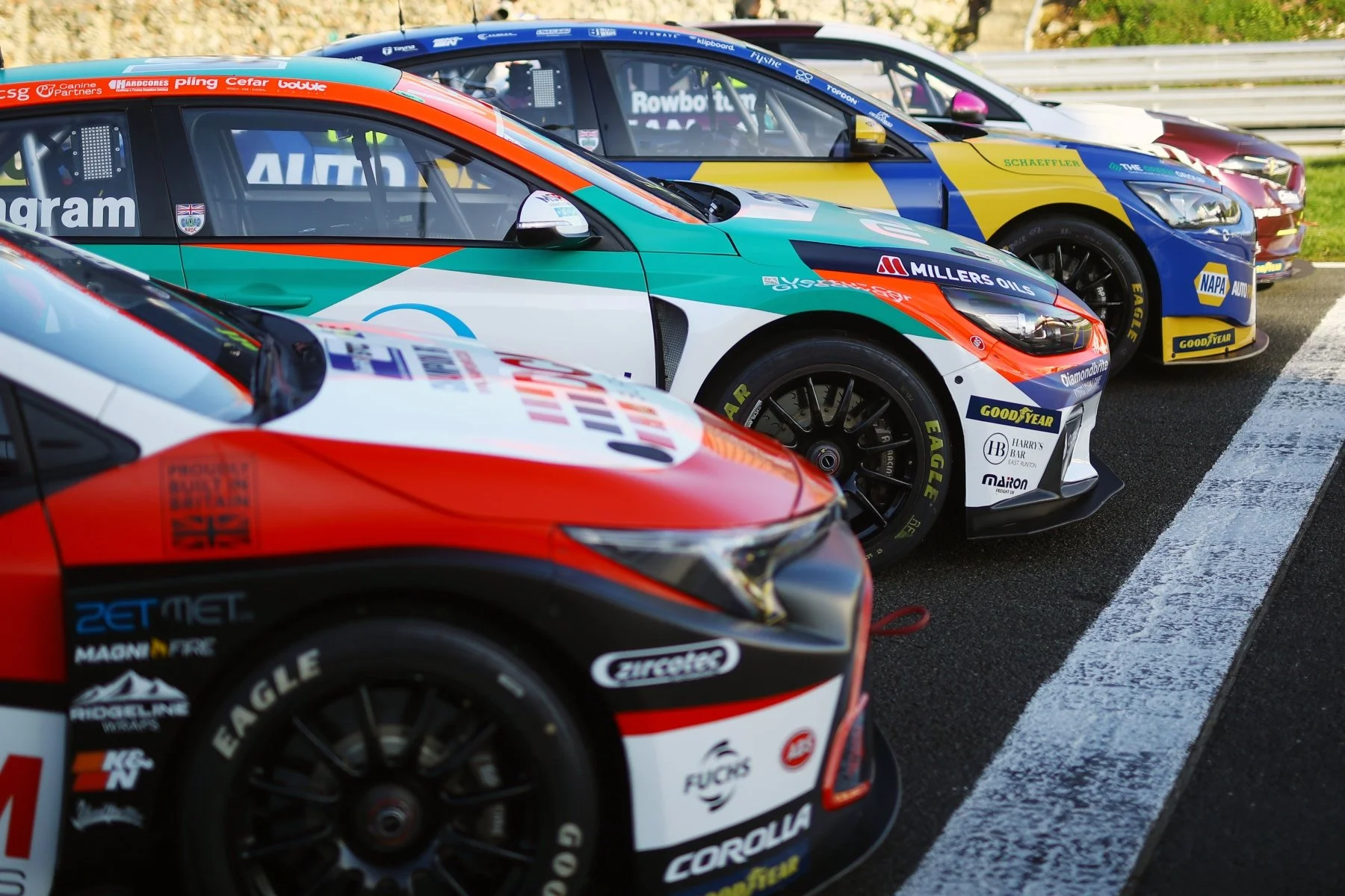 Race cars parked on a racetrack, featuring various sponsorship logos.