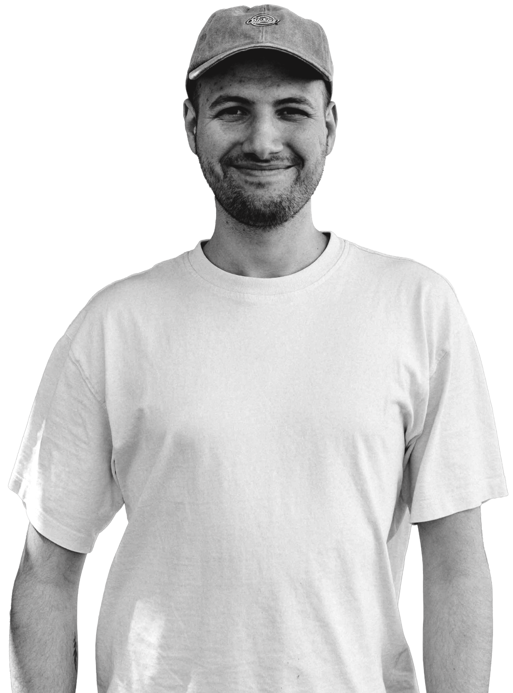 A young man (, smiling, wearing a baseball cap and a plain white t-shirt, standing against a black background.