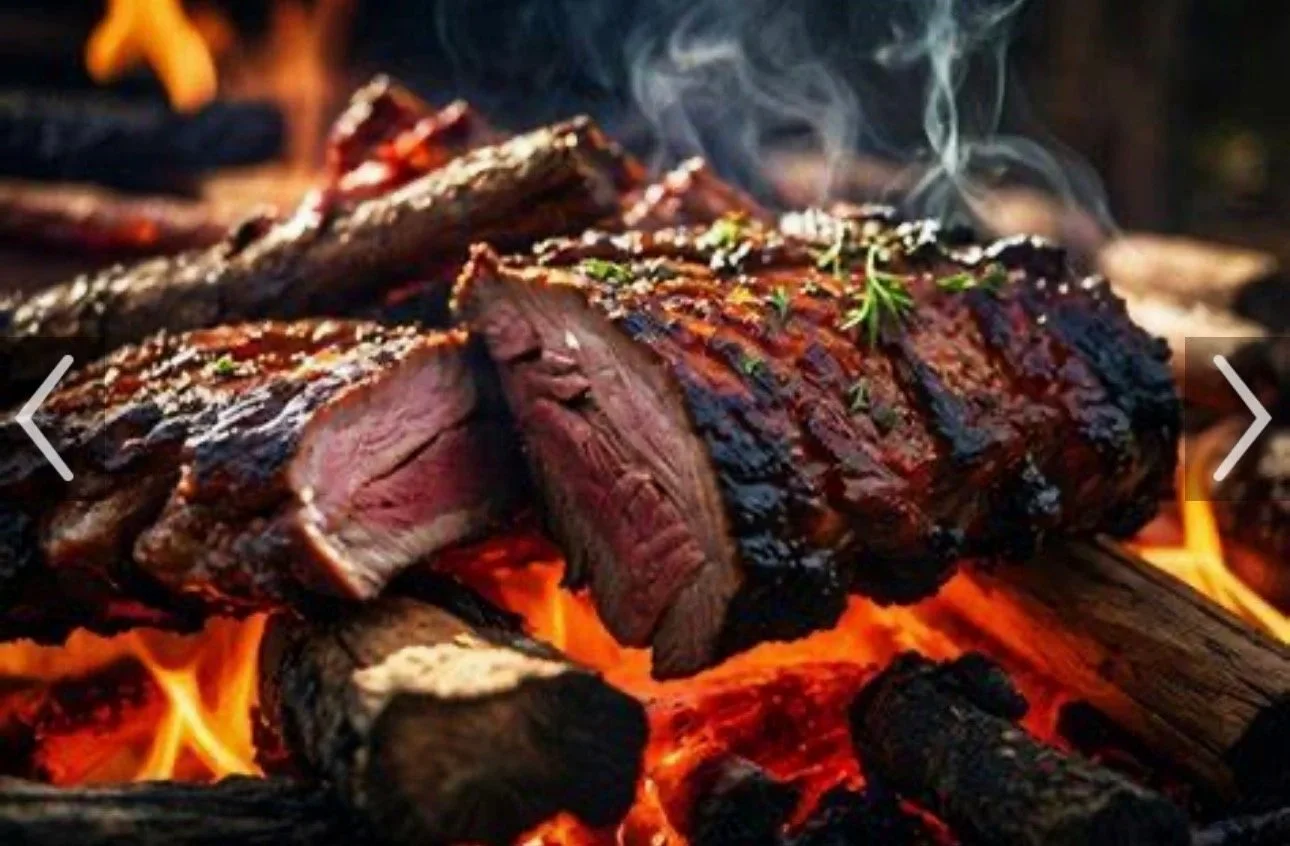 Close-up of a cooked, grilled steak with grill marks, garnished with herbs, on burning charcoal with visible orange flames and smoke.