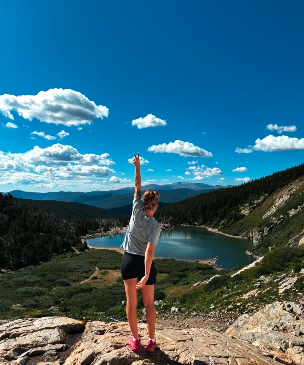 Andrea facing away towards the mountains raising one arm in the air