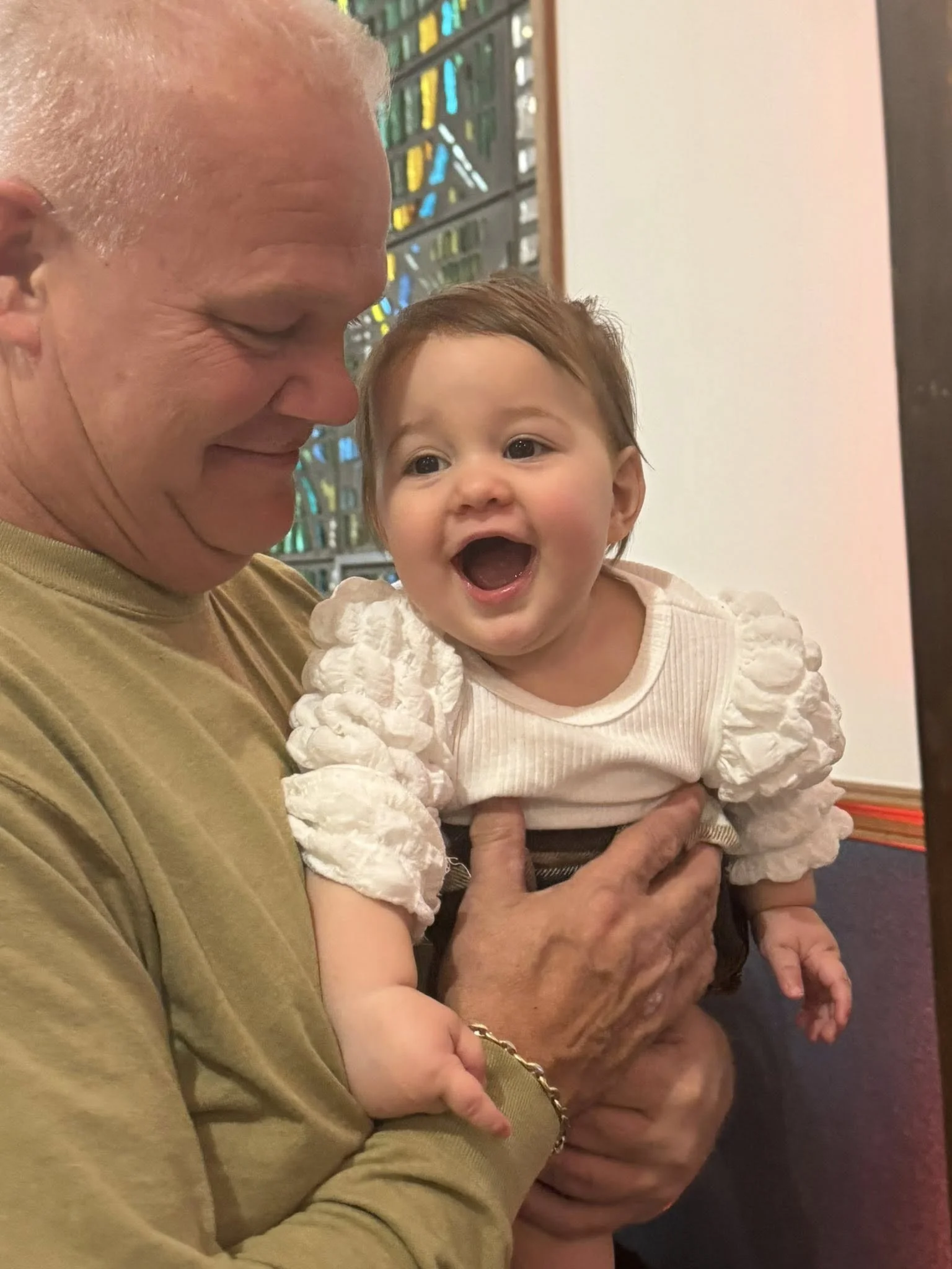 A smiling grandfather holding a happy young girl in a church with stained glass windows.